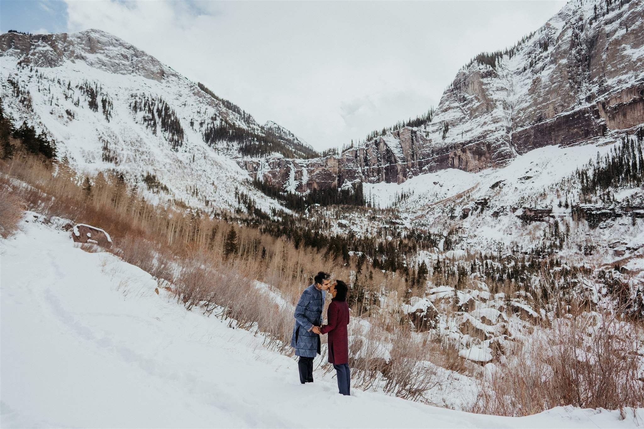 Two grooms kissing in the Colorado mountains for their winter elopement