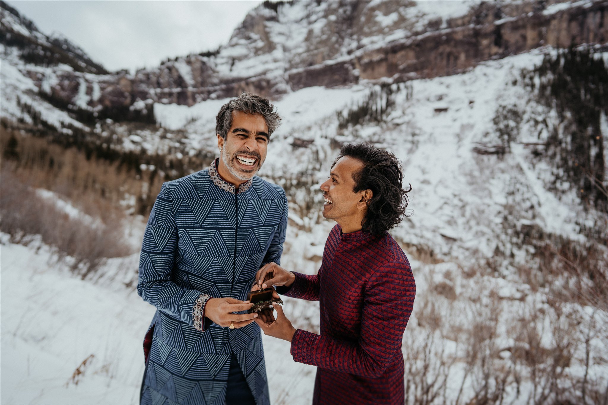 Two grooms laughing and exchanging rings at their winter elopement in the Colorado mountains