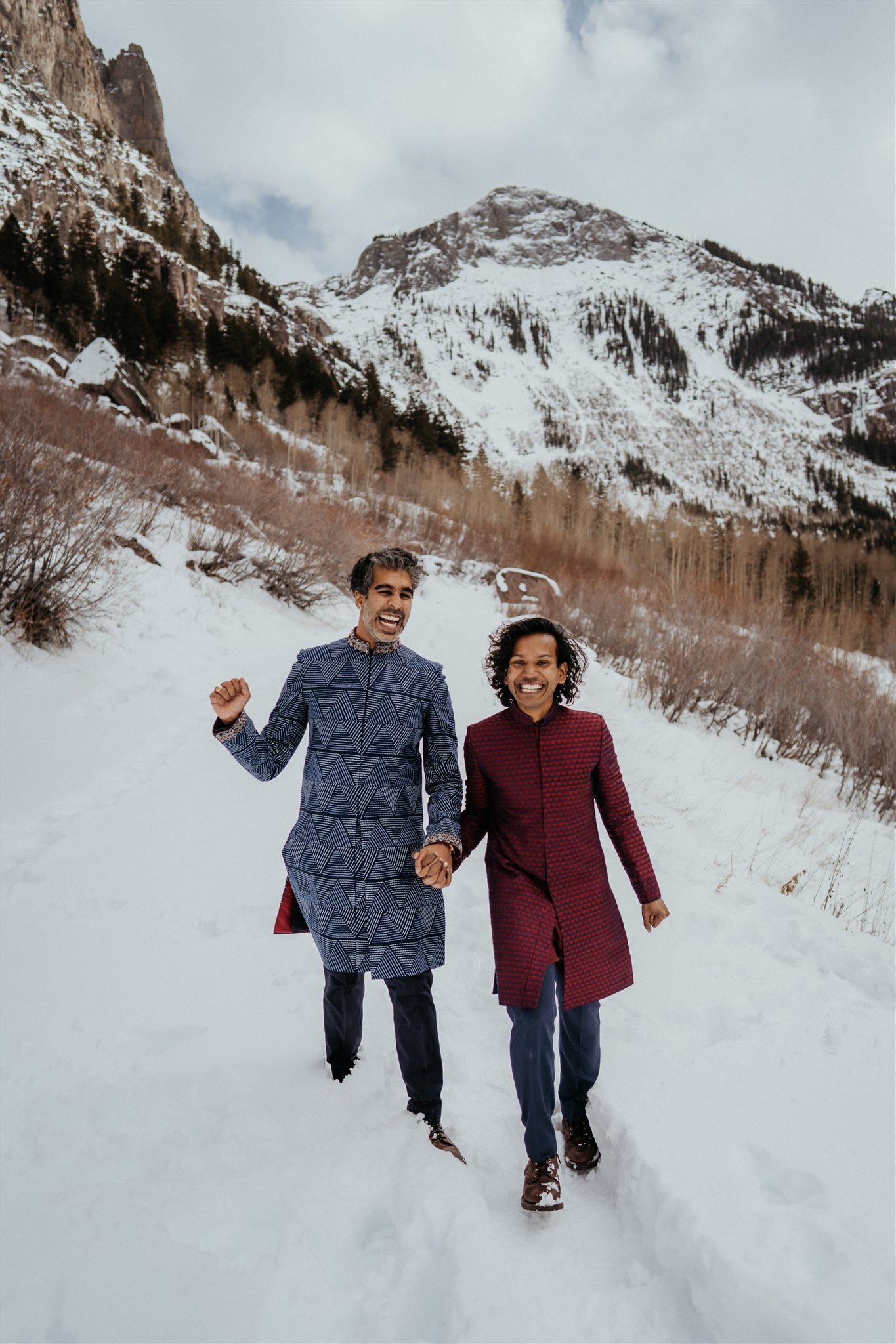 Two grooms holding hands and cheering as they walk down the Colorado mountains after their elopement