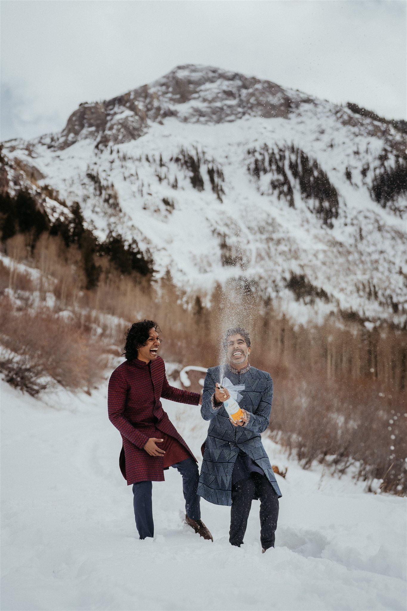 Two grooms popping champagne in the Colorado mountains
