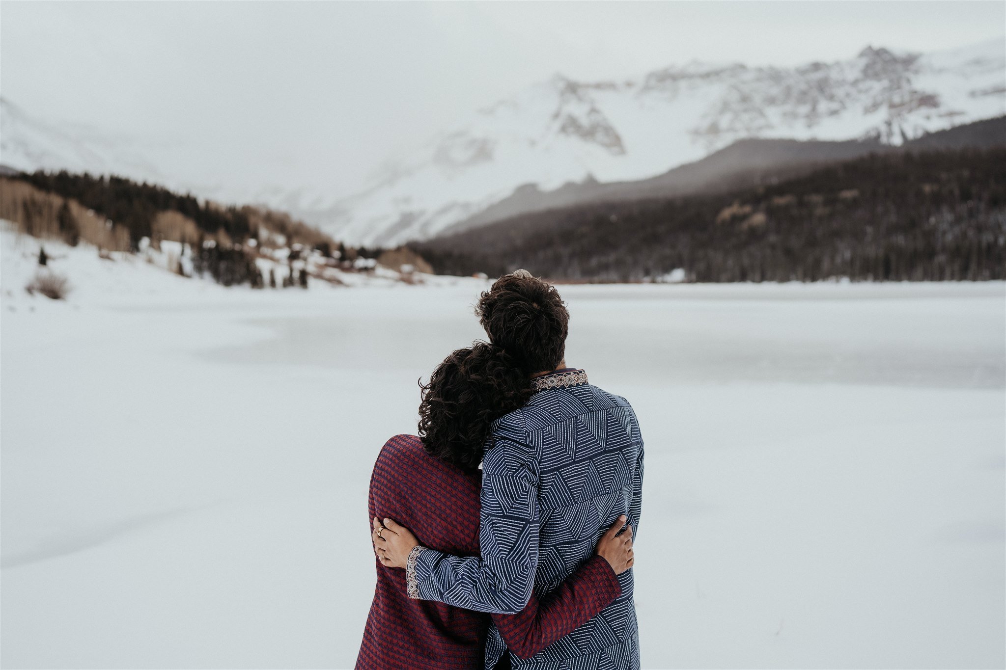 Two grooms hugging looking out at the snowy Colorado mountains 