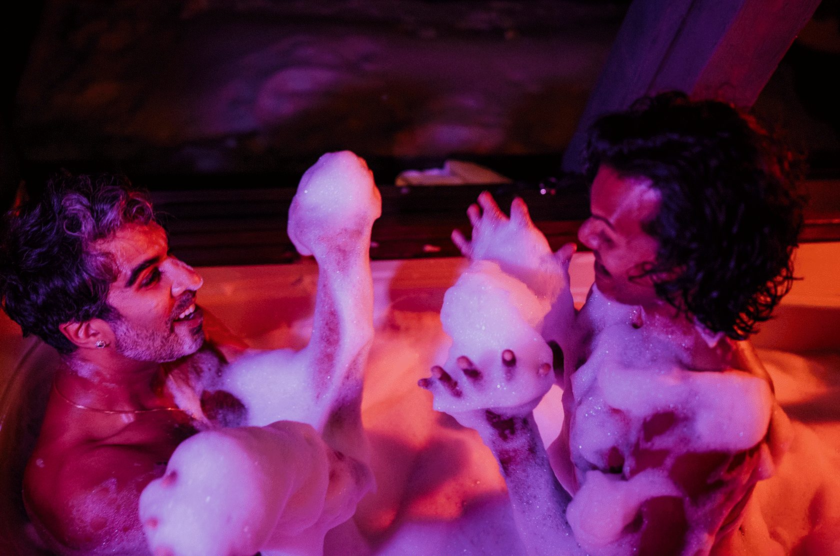 Two grooms splashing bubbles in a hot tub after their winter elopement