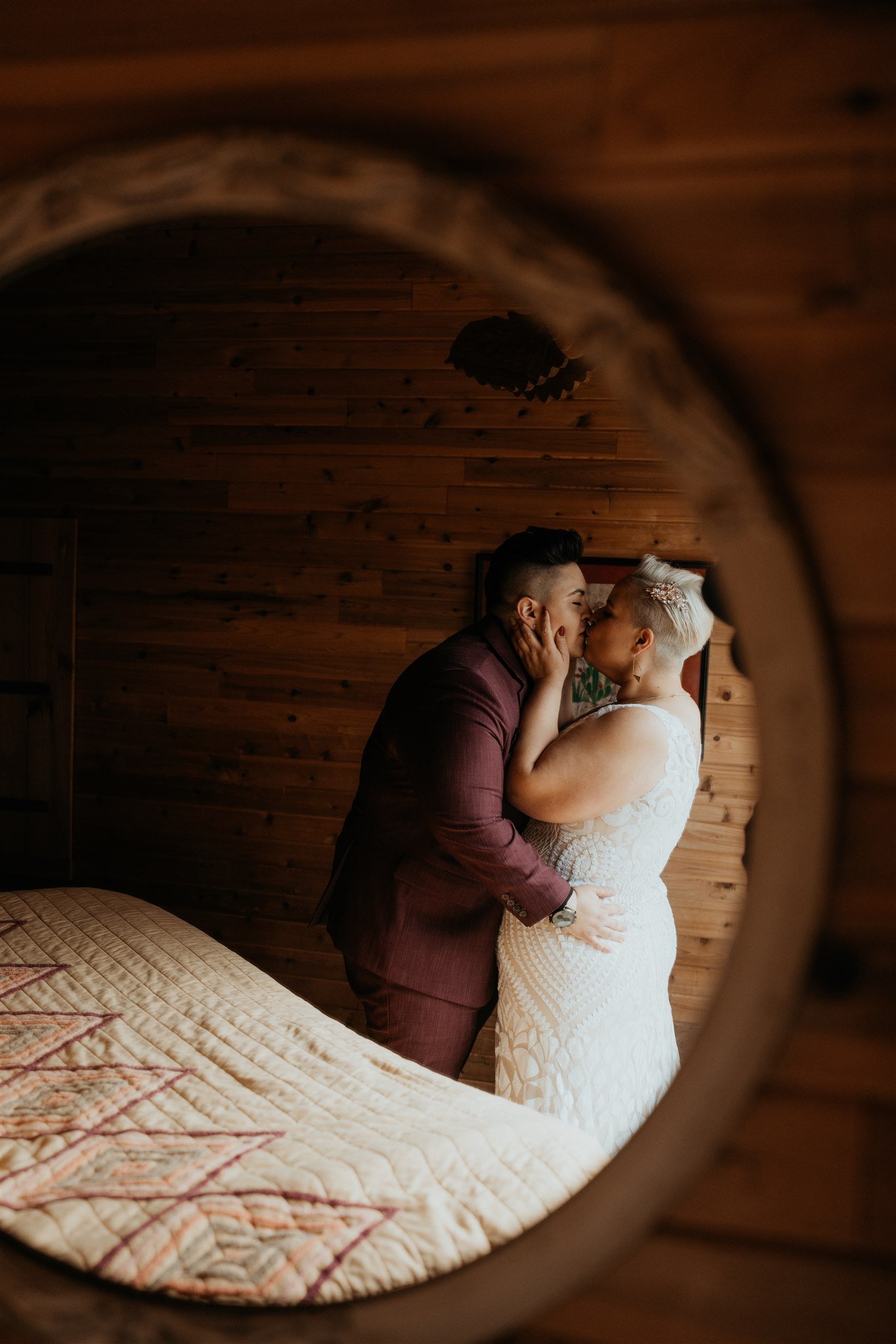 Two brides kiss in front of round mirror at PNW elopement cabin