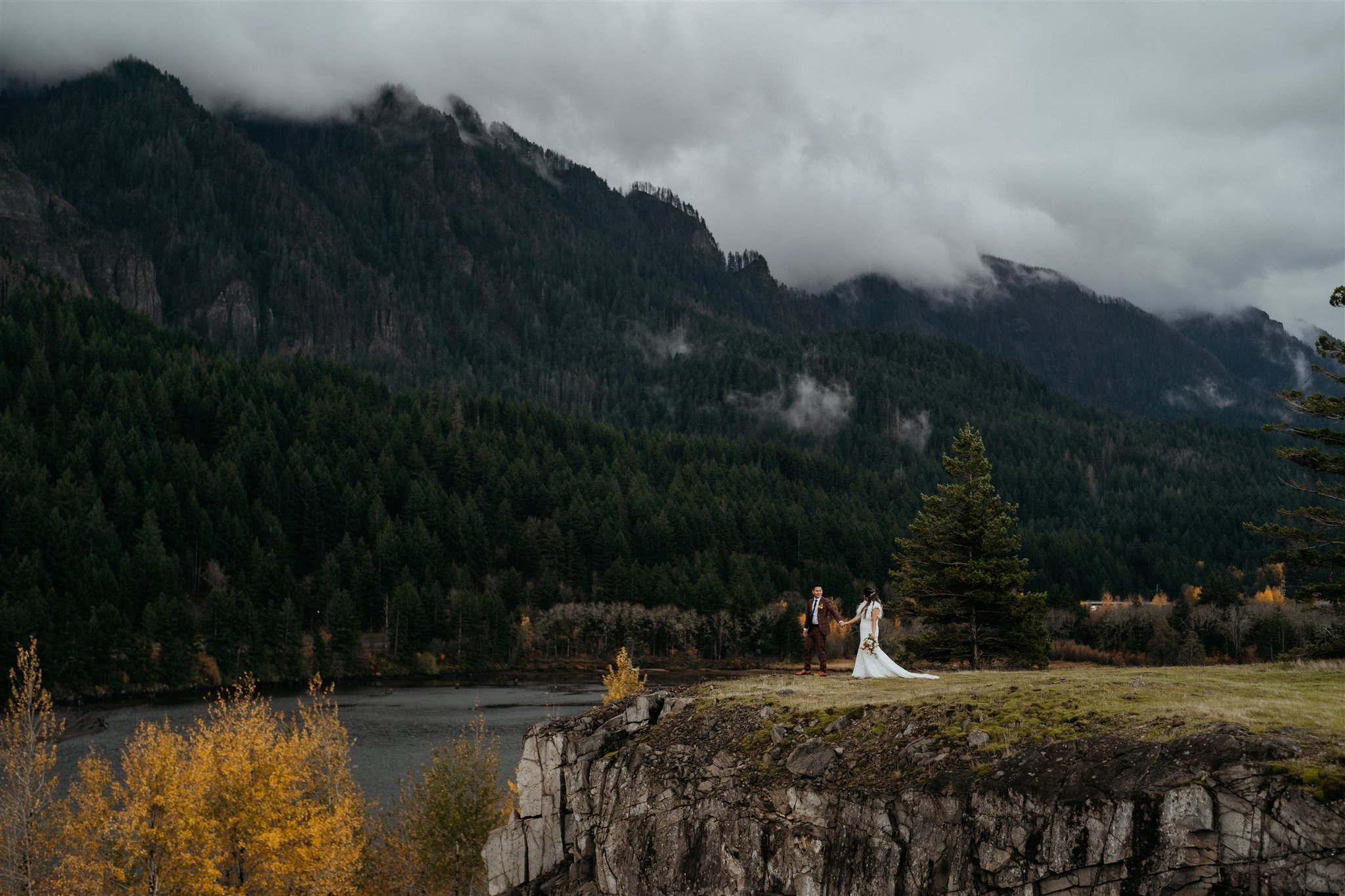 Bride and groom hold hands while walking to the edge of cliff in Oregon