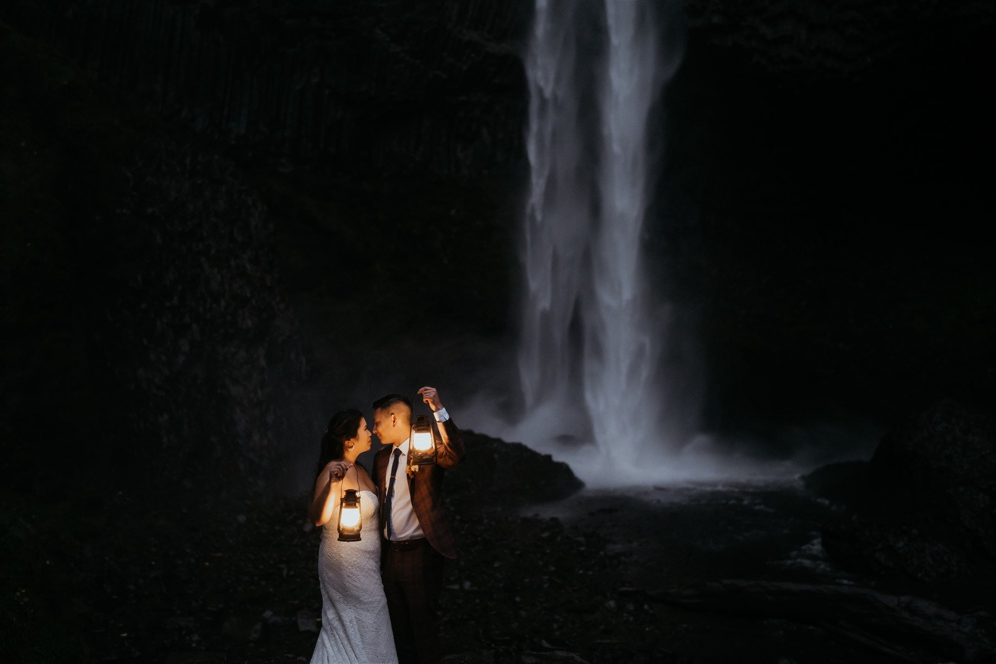 Bride and groom kiss while holding lanterns at Oregon waterfall wedding