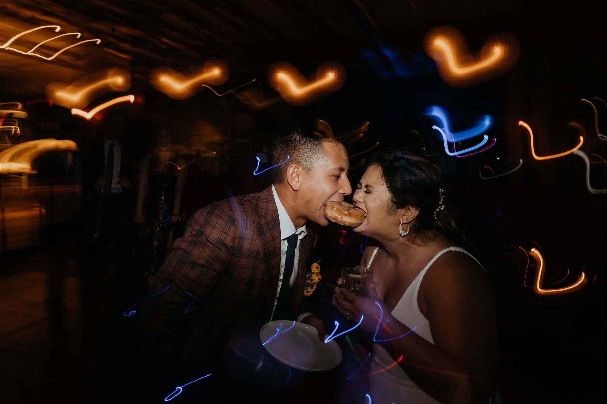 Bride and groom biting into doughnut during wedding reception in Portland