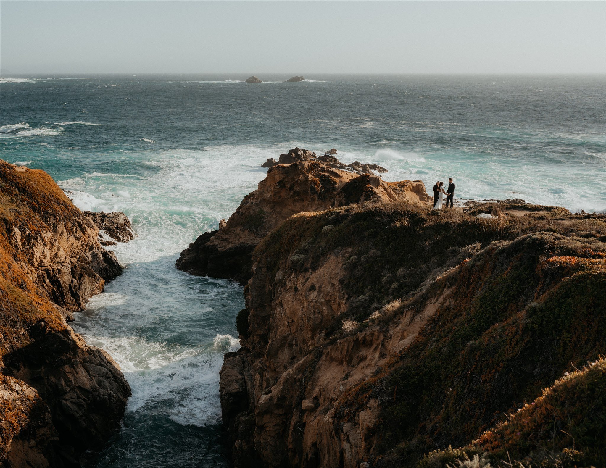 Bride and groom standing on the edge of a cliff at Big Sur elopement location