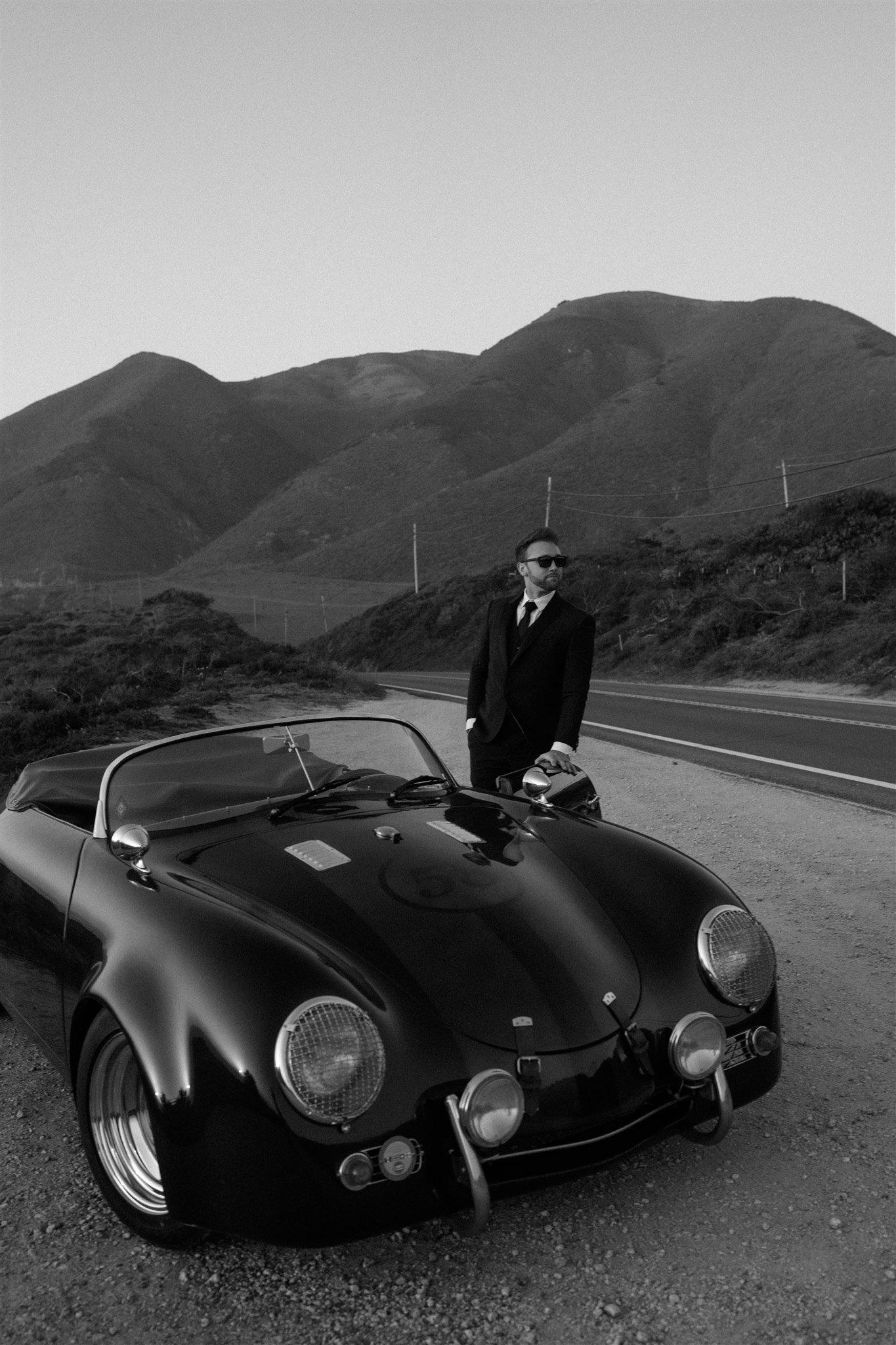 Groom standing next to vintage convertible car on the side of the road in Big Sur