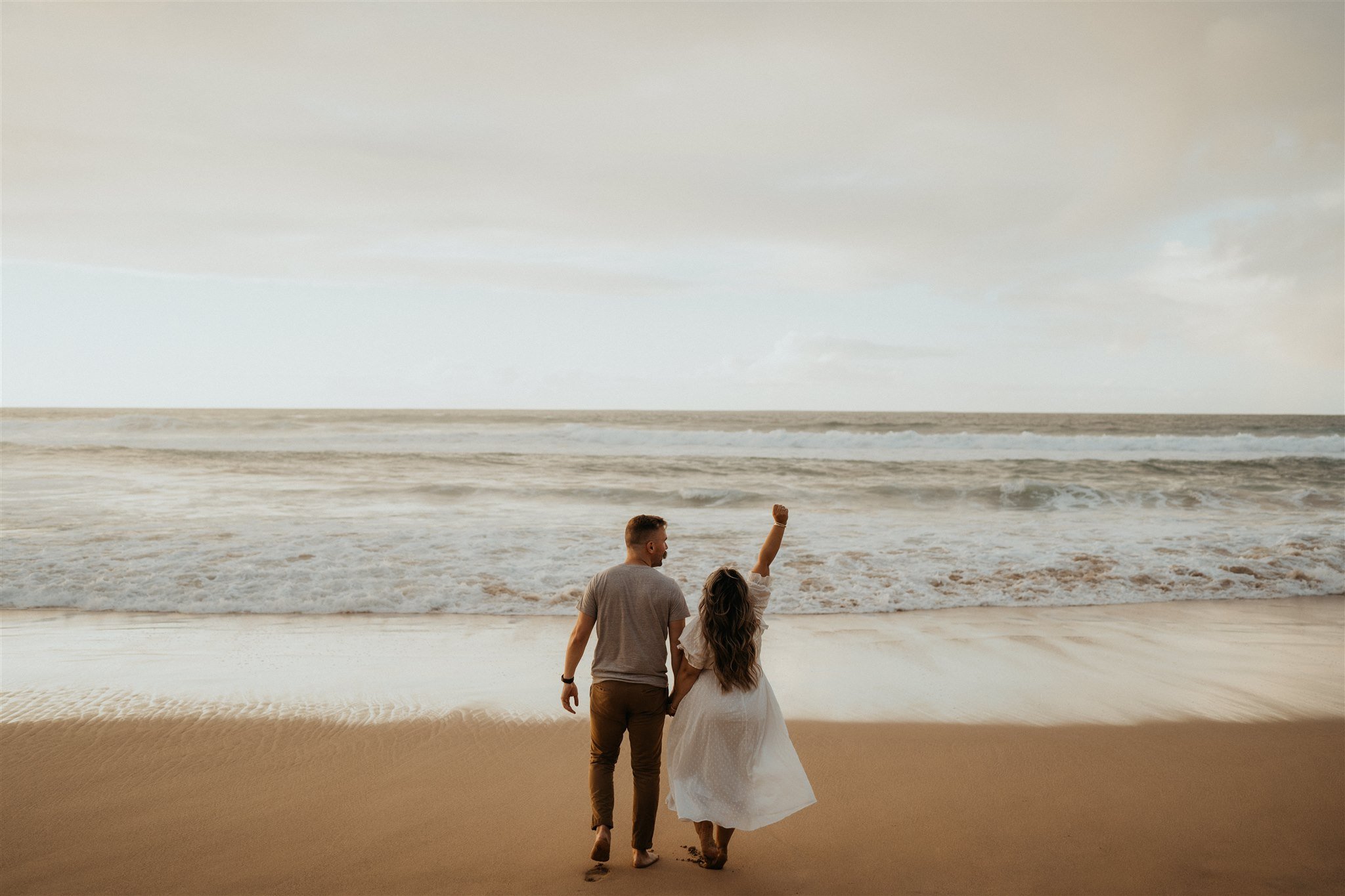 Couple running across the beach during Hawaii engagement photo session