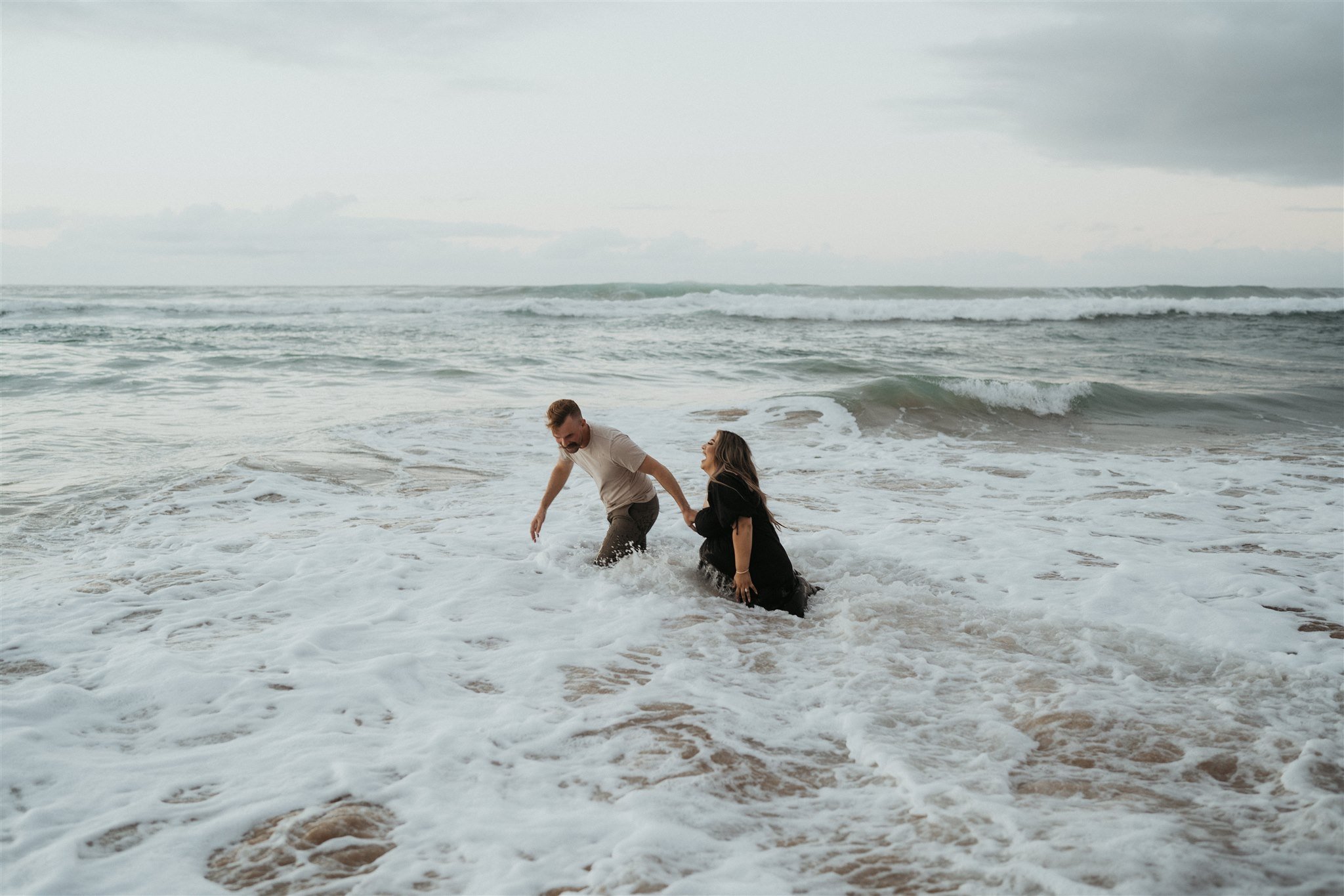 Couple running into the ocean during Hawaii engagement photos