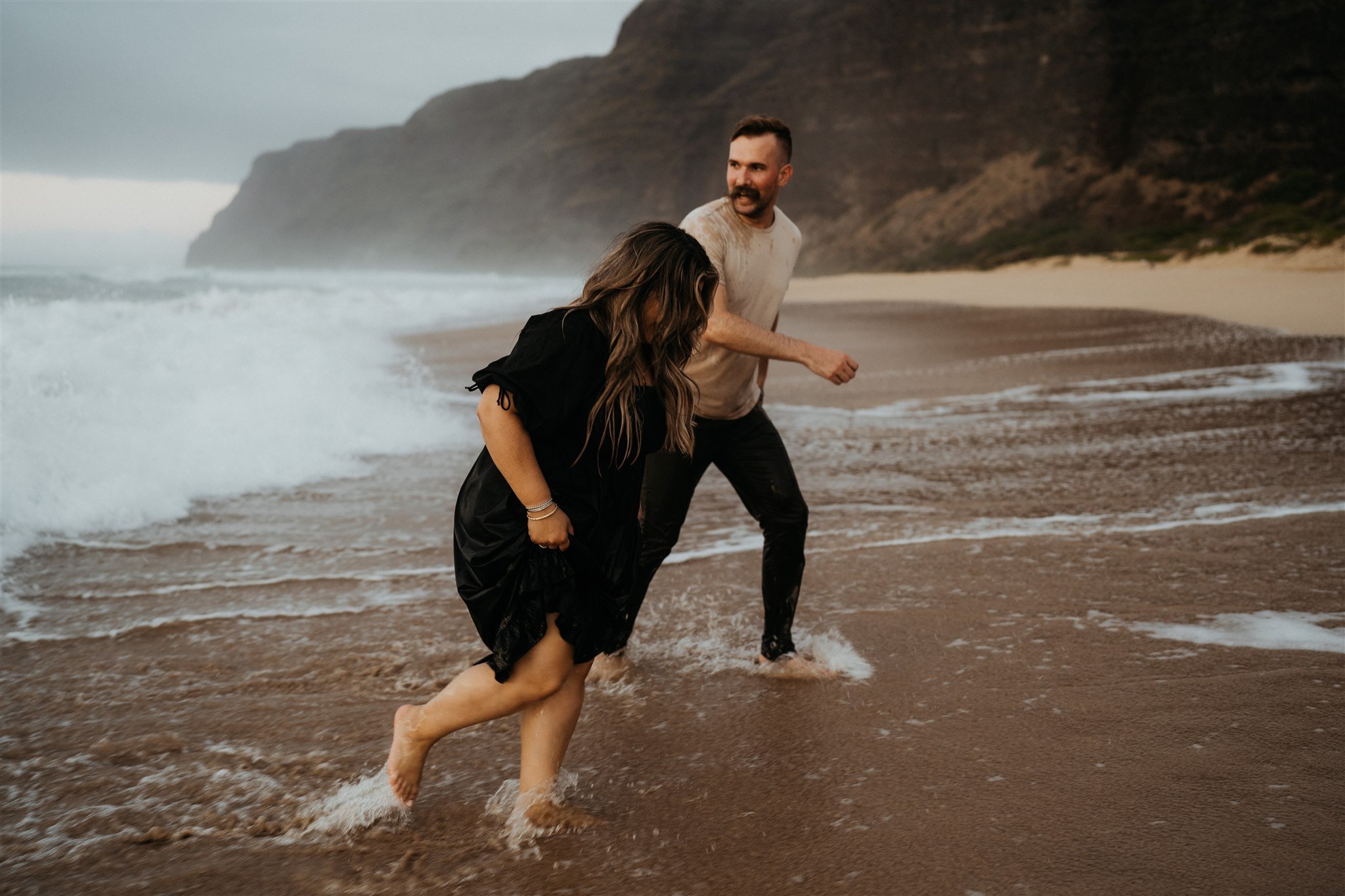 Couple running away from the ocean during Hawaii engagement photos