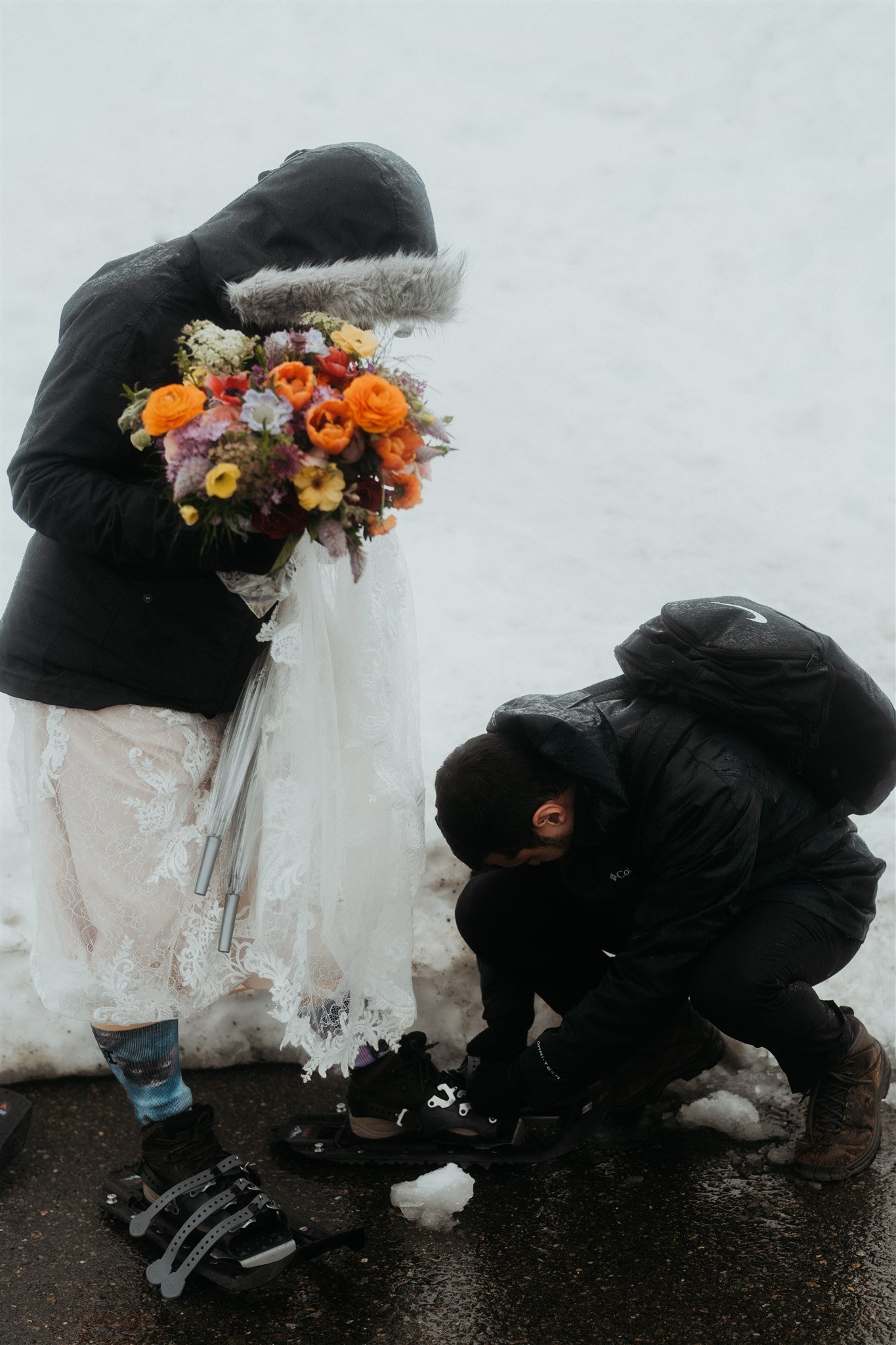 Groom helping bride put on snowshoes for hiking elopement in the Washington mountains