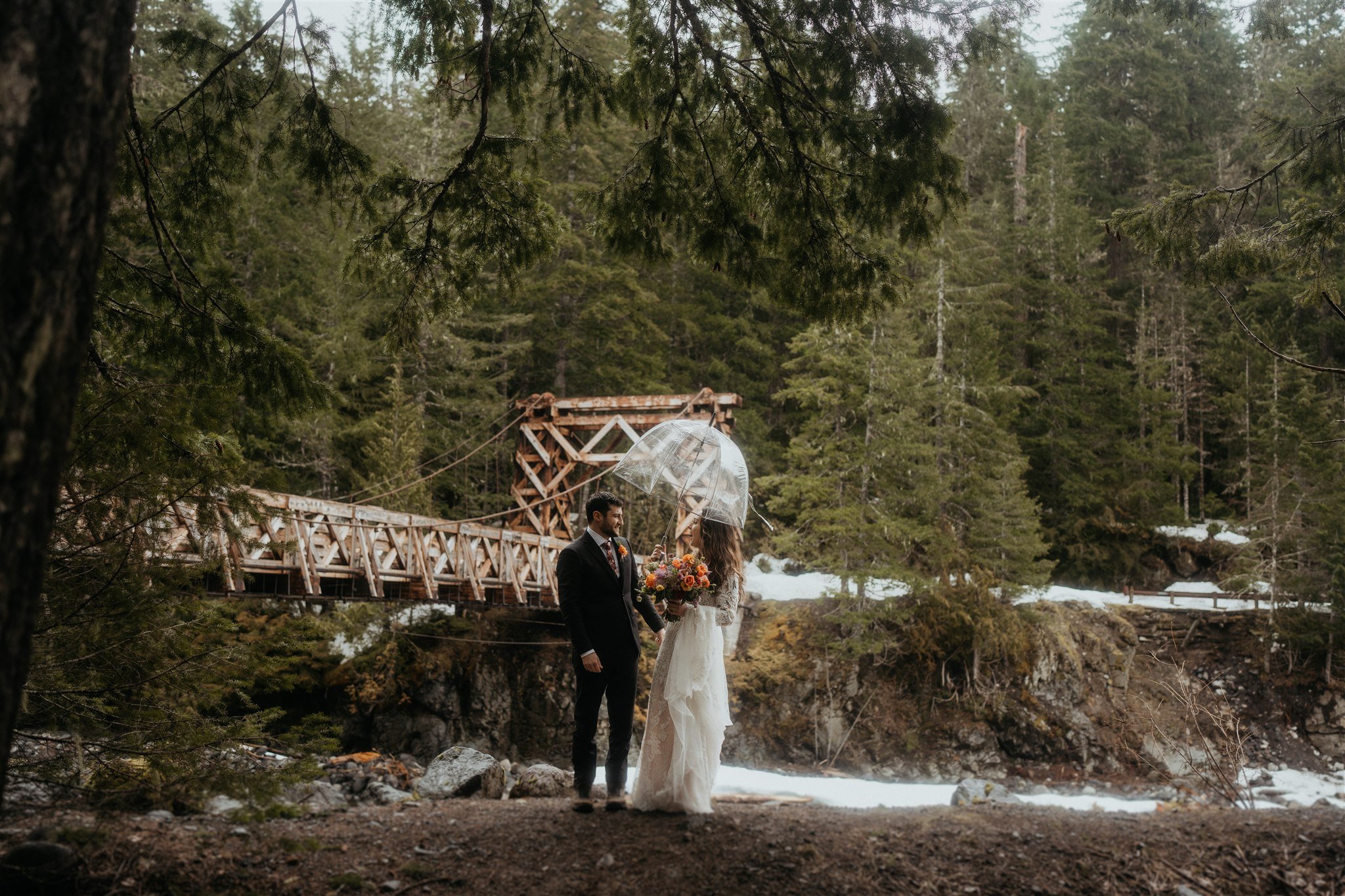 Bride and groom holding an umbrella during snowy mountain elopement at Mt Rainier