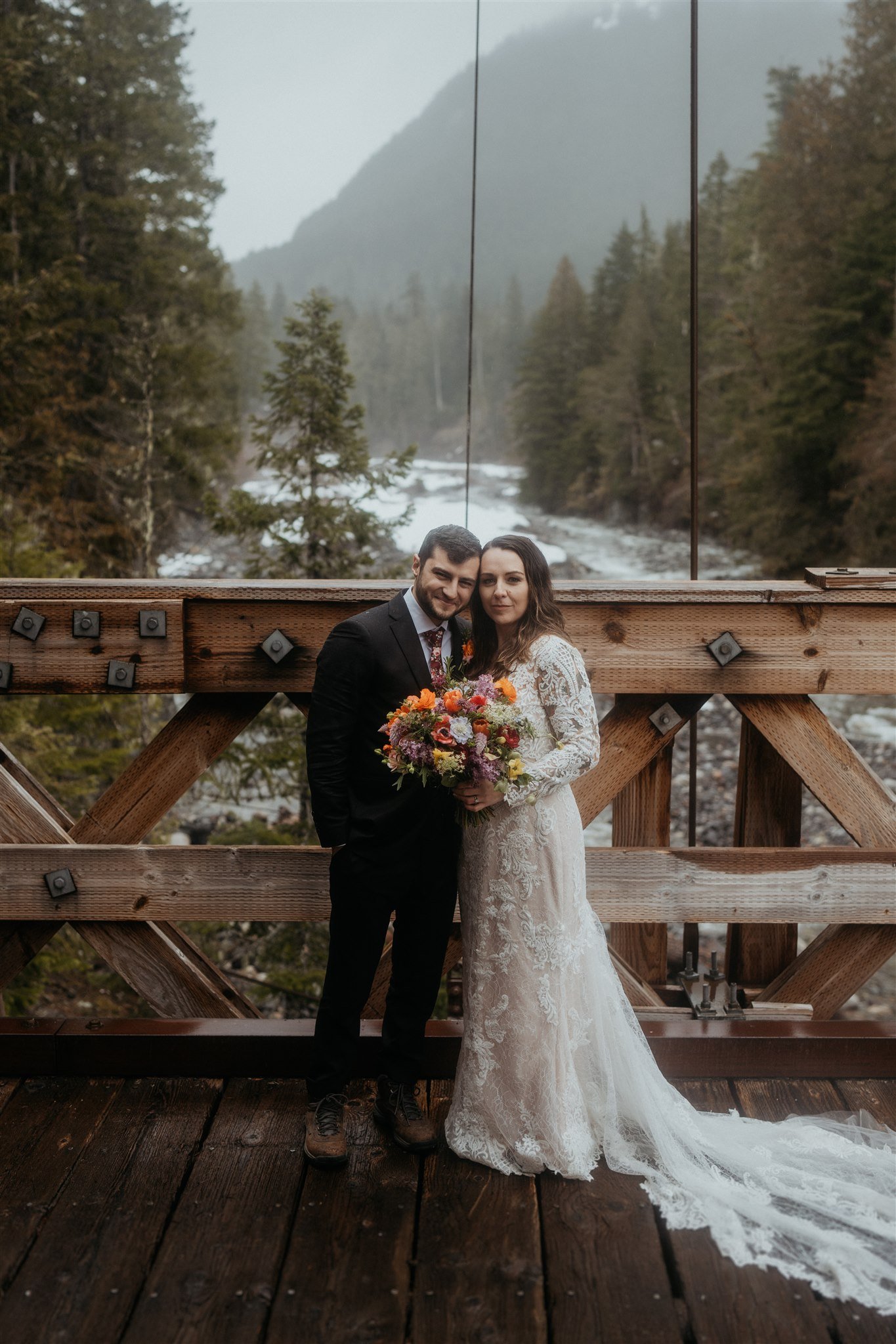 Bride and groom standing on a bridge near Mt Rainier for their snowy mountain elopement