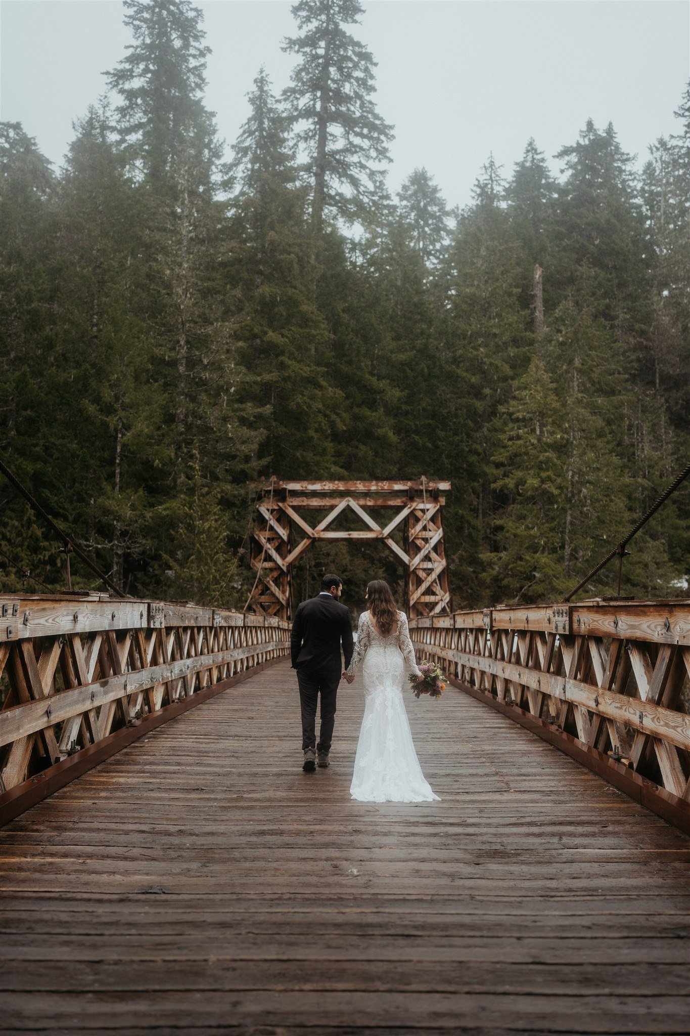 Bride and groom walking on a bridge near Mt Rainier for their snowy mountain elopement