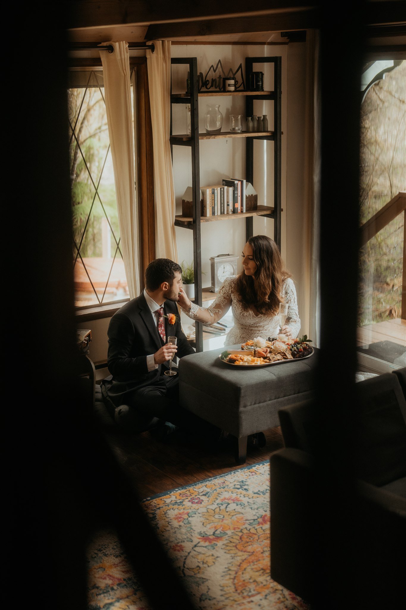 Bride and groom sit on the floor eating a cheese board after their snowy mountain elopement in Washington