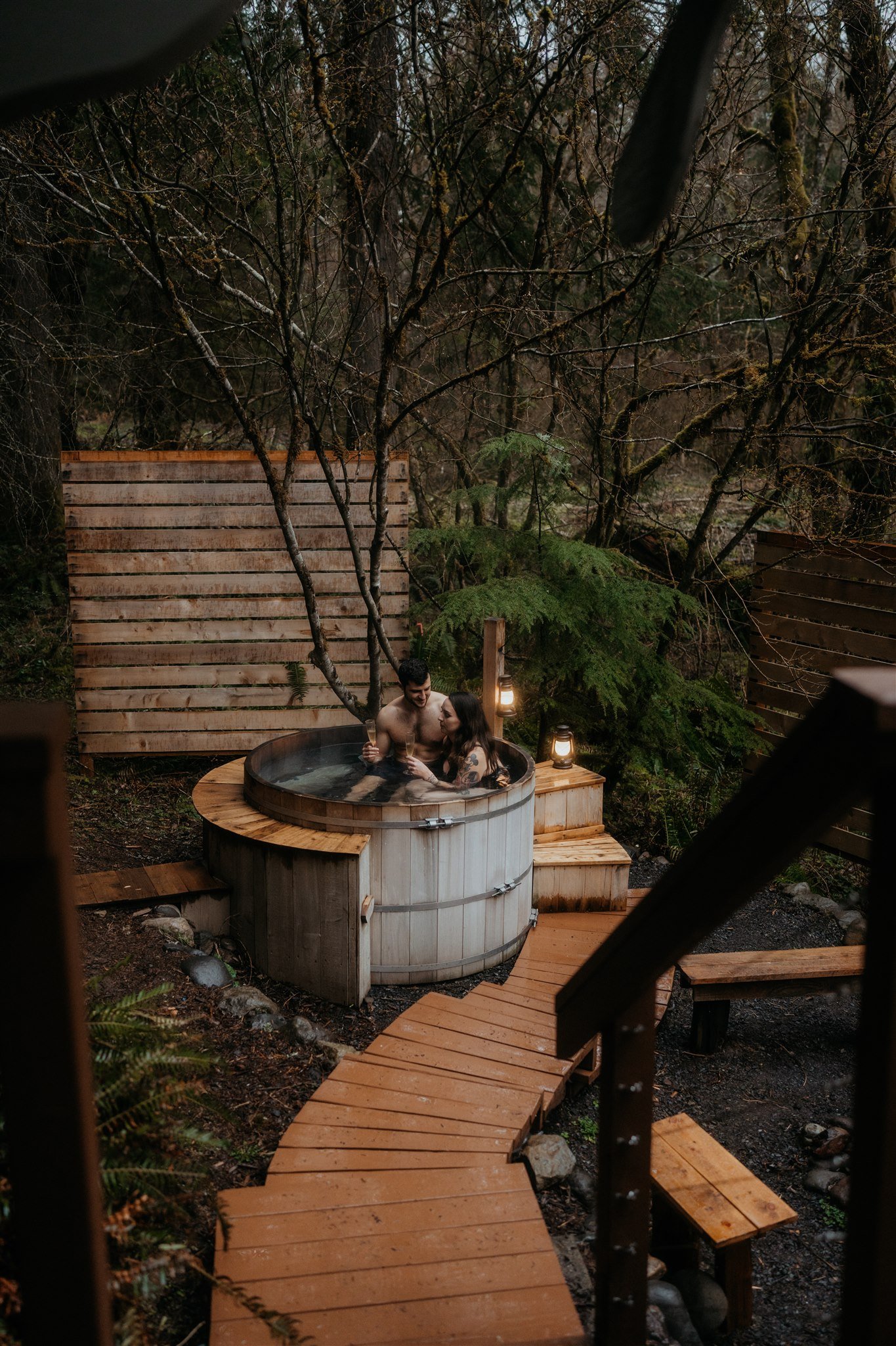 Bride and groom drink champagne in barrel hot tub after snowy hiking elopement