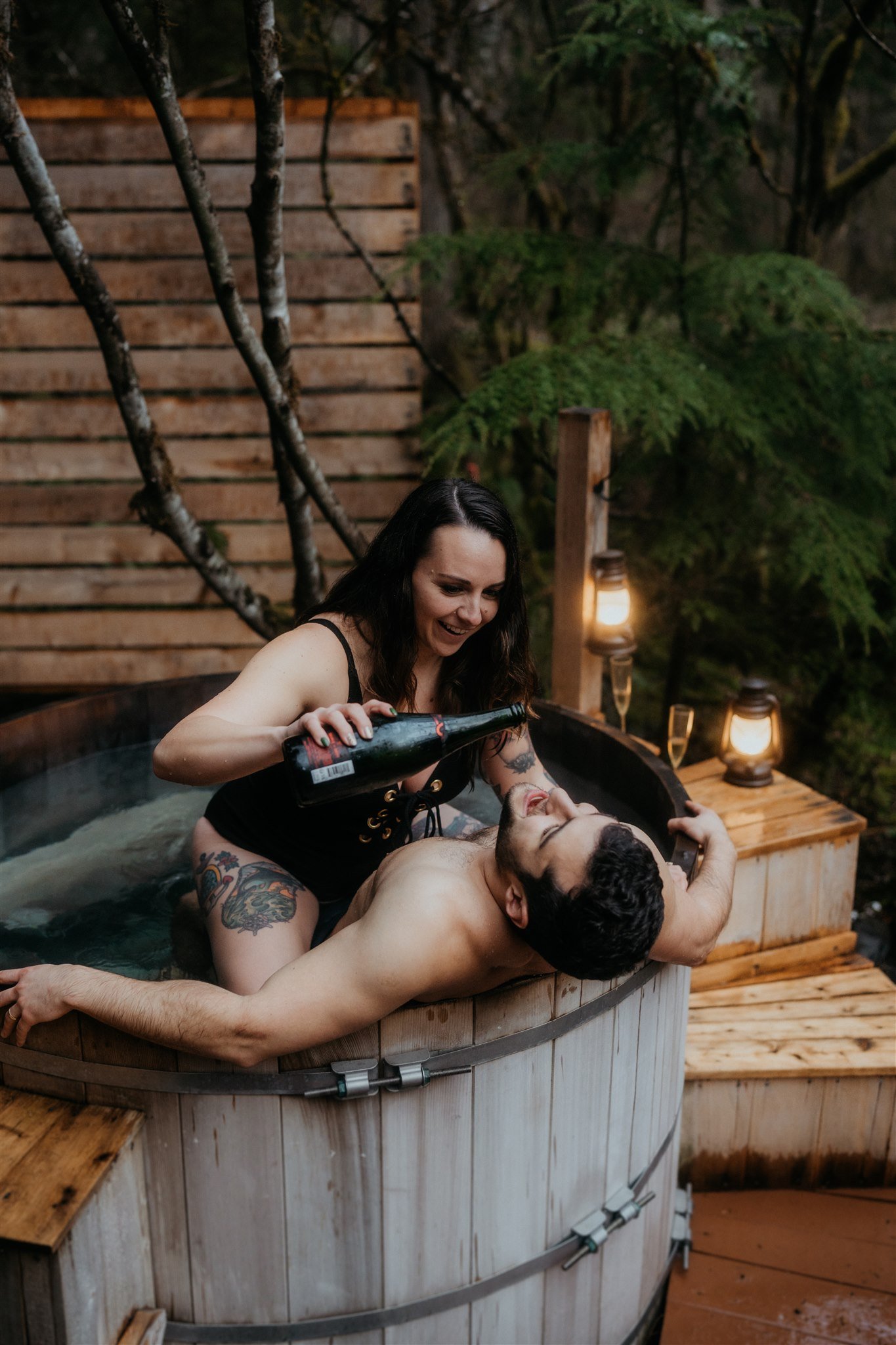 Bride and groom drink champagne in barrel hot tub after snowy hiking elopement