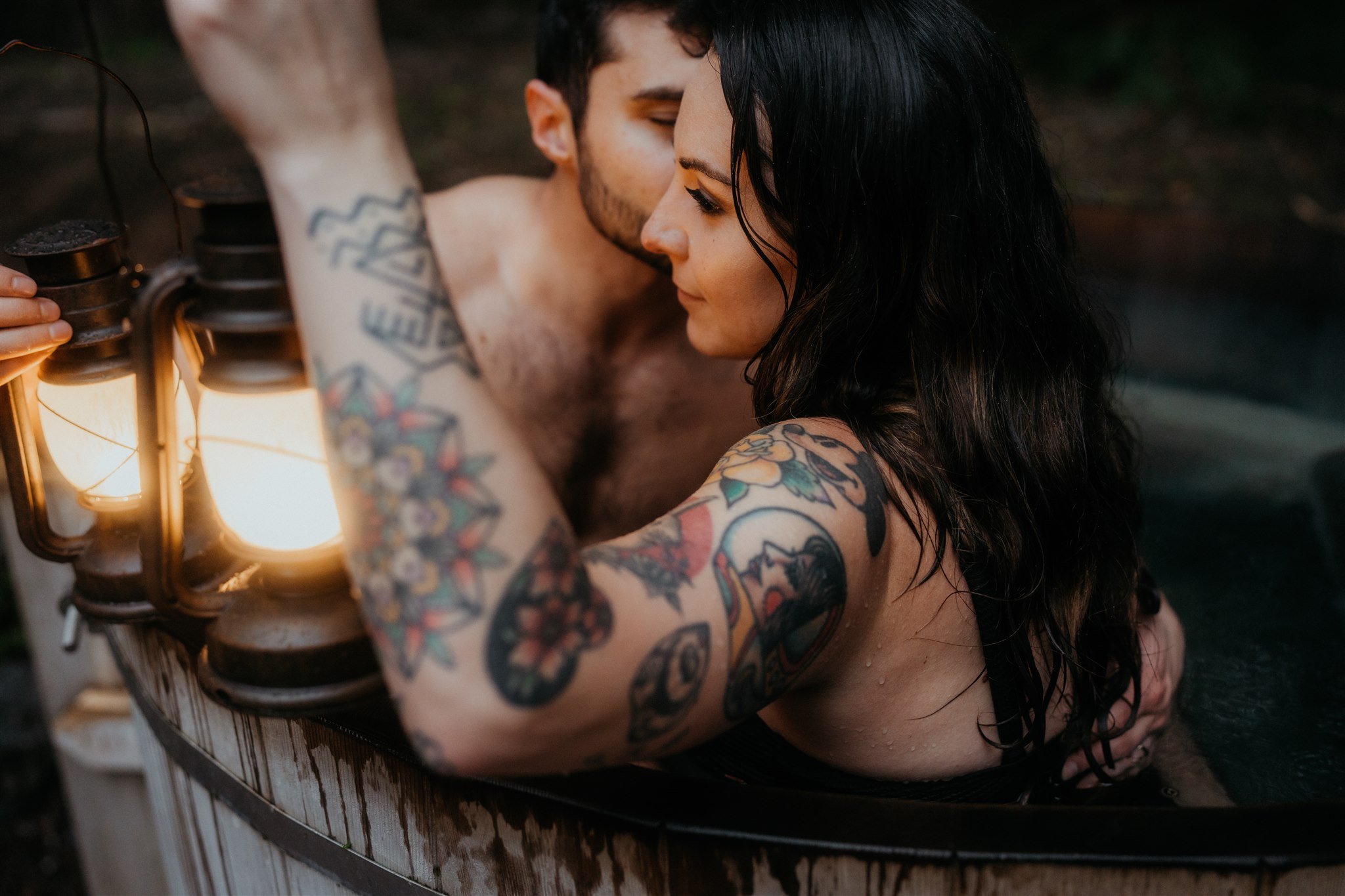 Bride and groom holding lanterns in barrel hot tub after snowy hiking elopement