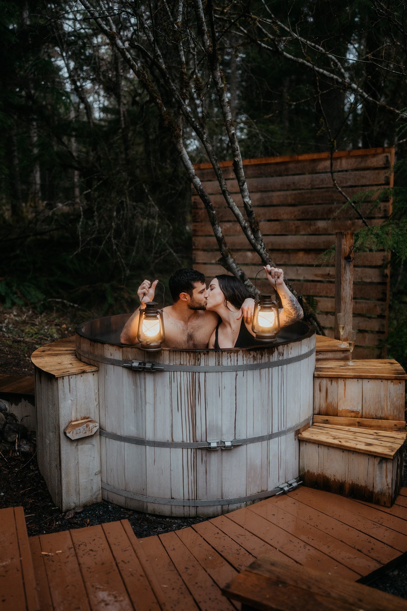 Bride and groom holding lanterns in barrel hot tub after snowy hiking elopement