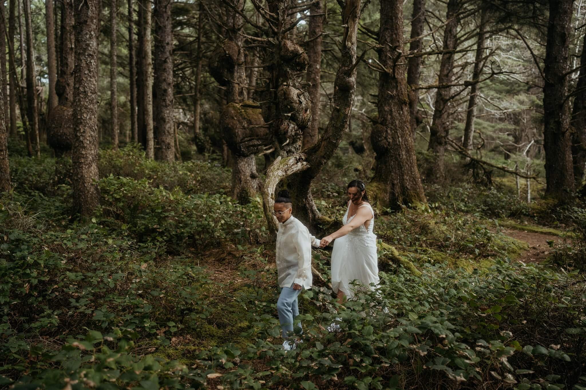 Two brides holding hands walking through the forest in Olympic National Park