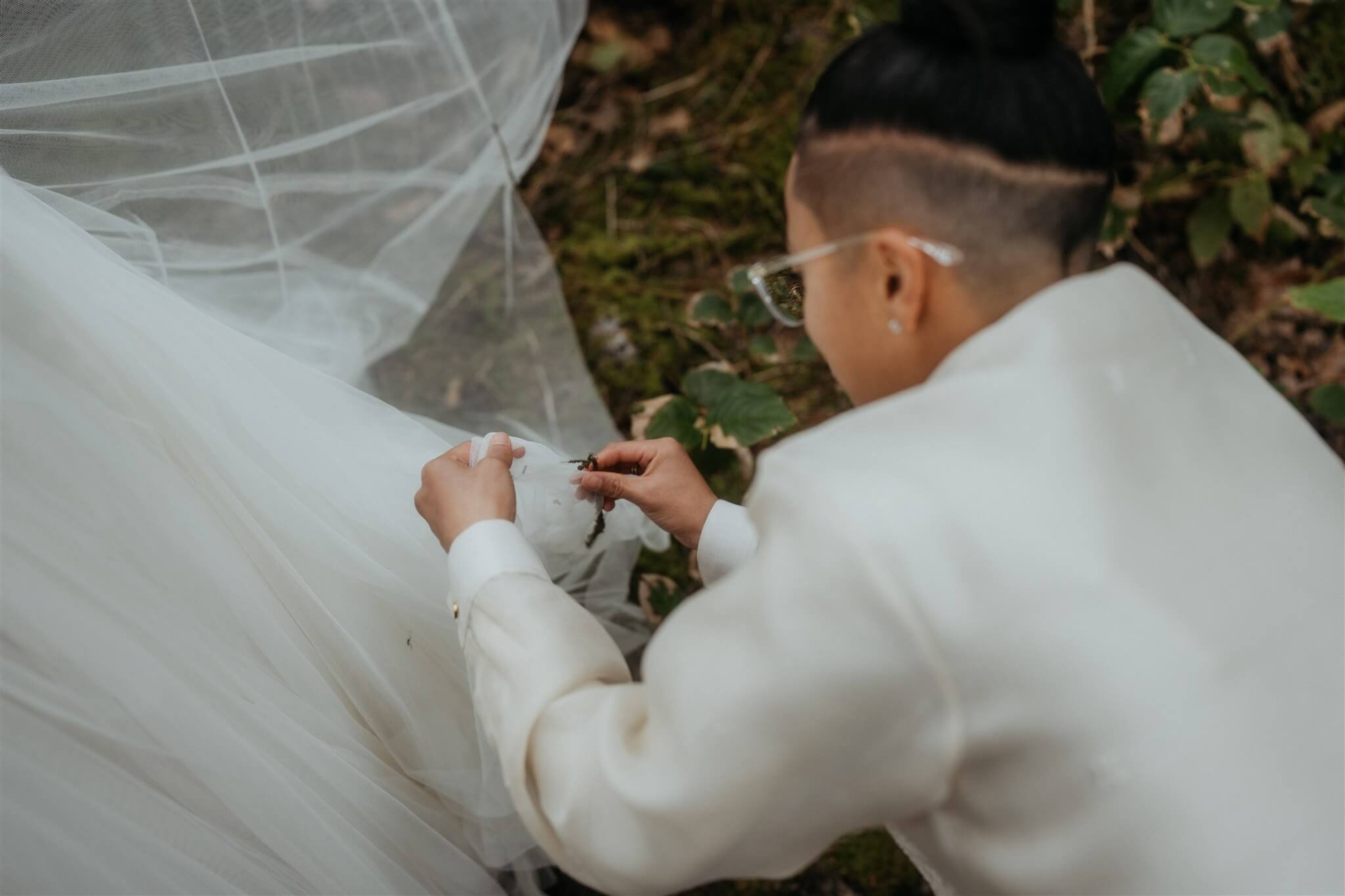 Bride picking sticks out of partner's wedding dress