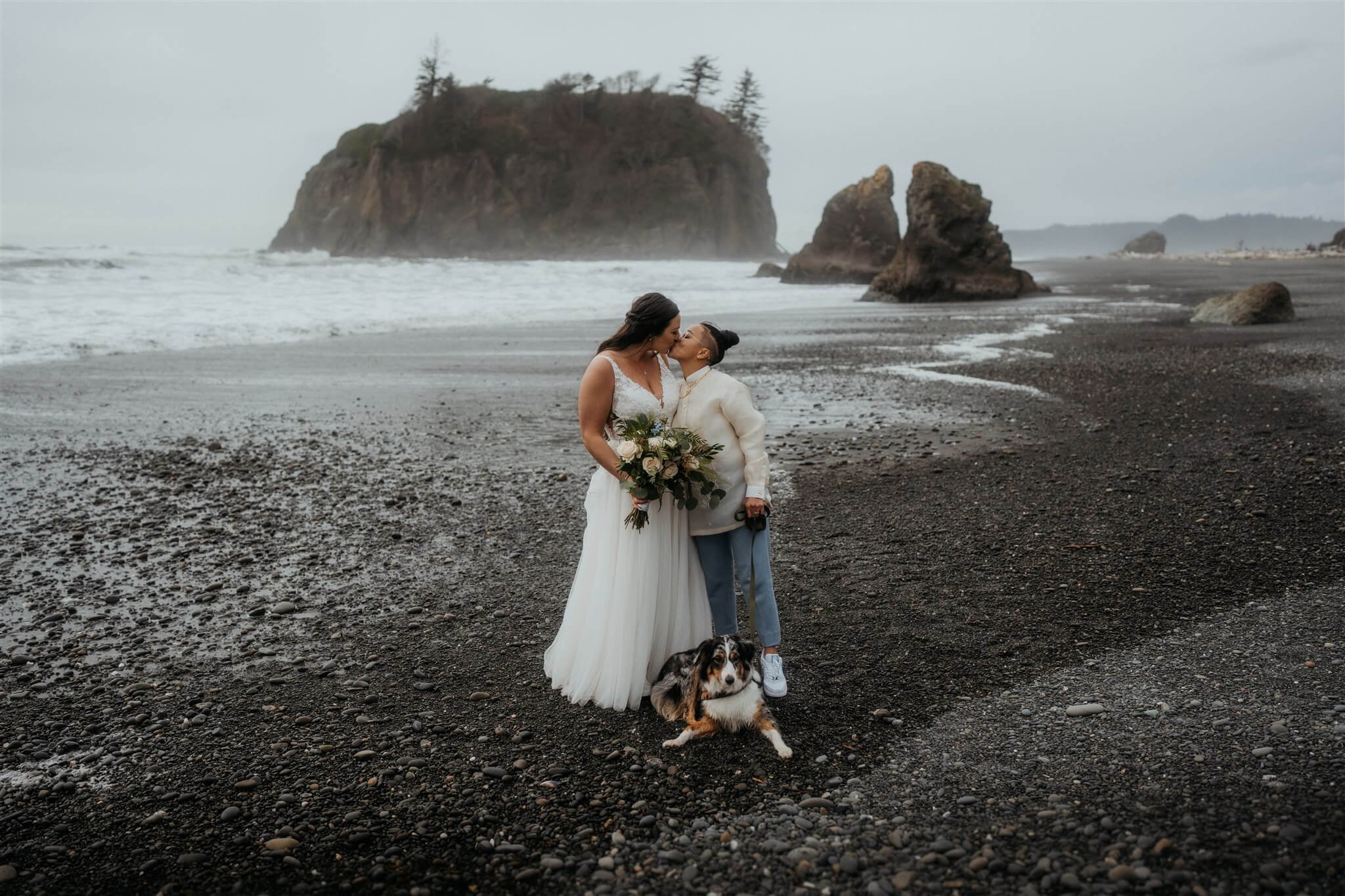 Brides kissing on Ruby Beach while dog lays at their feet
