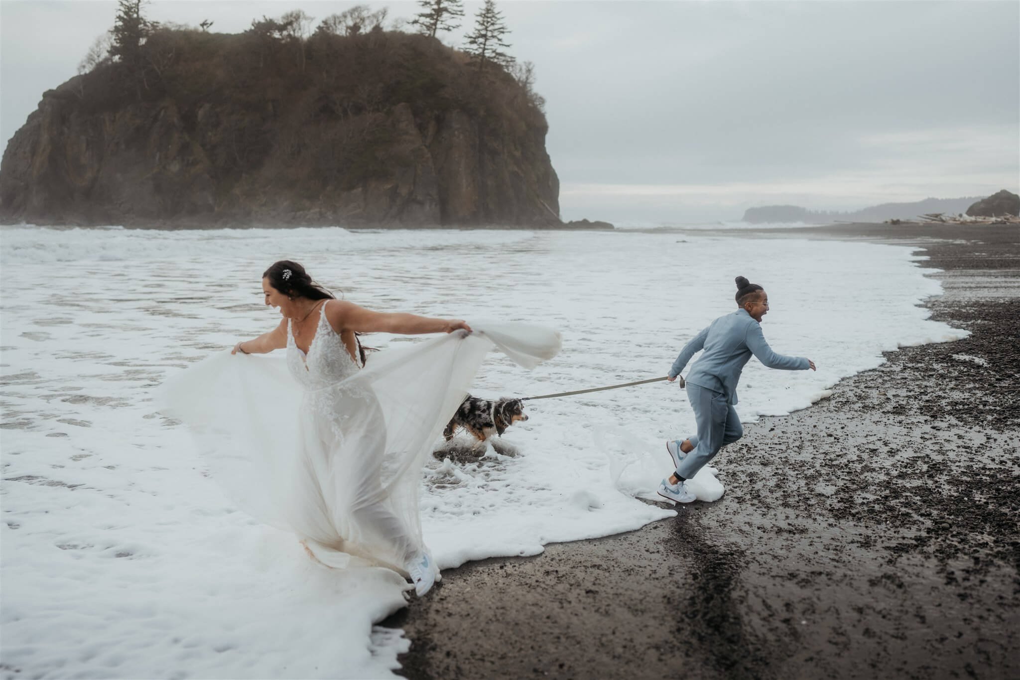 Brides and their dog running in the water at Ruby Beach