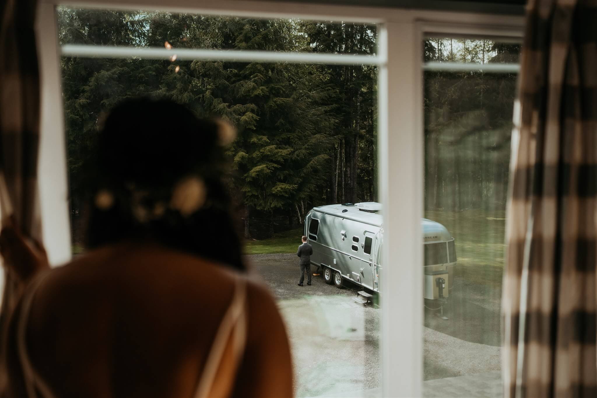 Bride looking out the window at groom standing next to airstream trailer