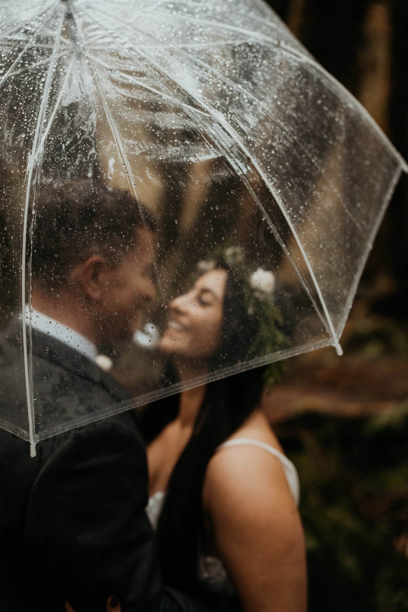 Bride and groom kiss under clear umbrella during Hoh Rainforest elopement