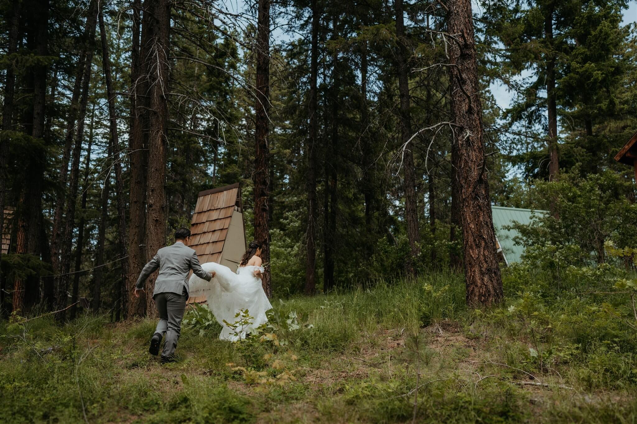 Groom holding wedding dress train while walking up the hill