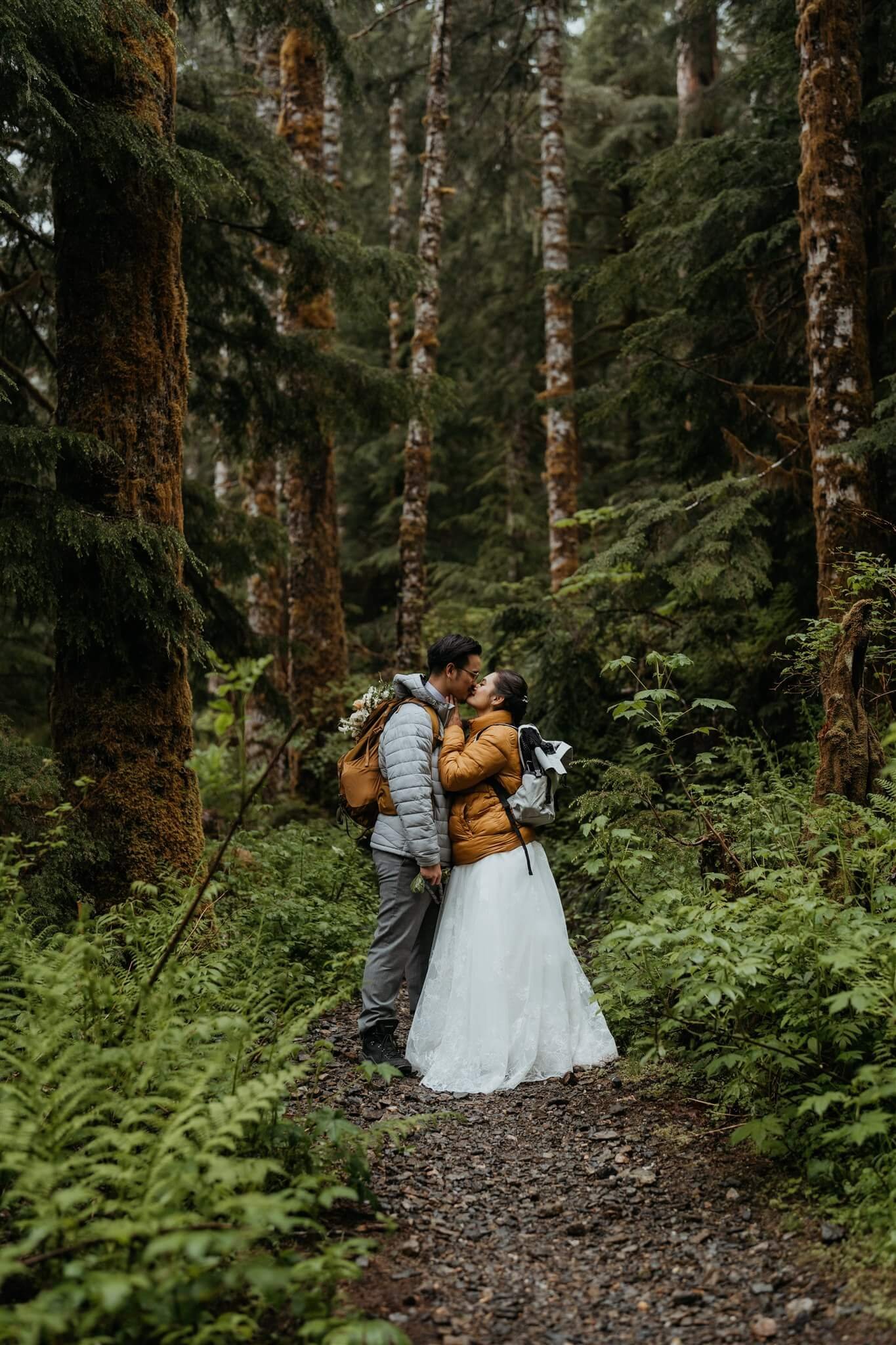 Bride and groom kiss in the forest while hiking to their elopement ceremony location