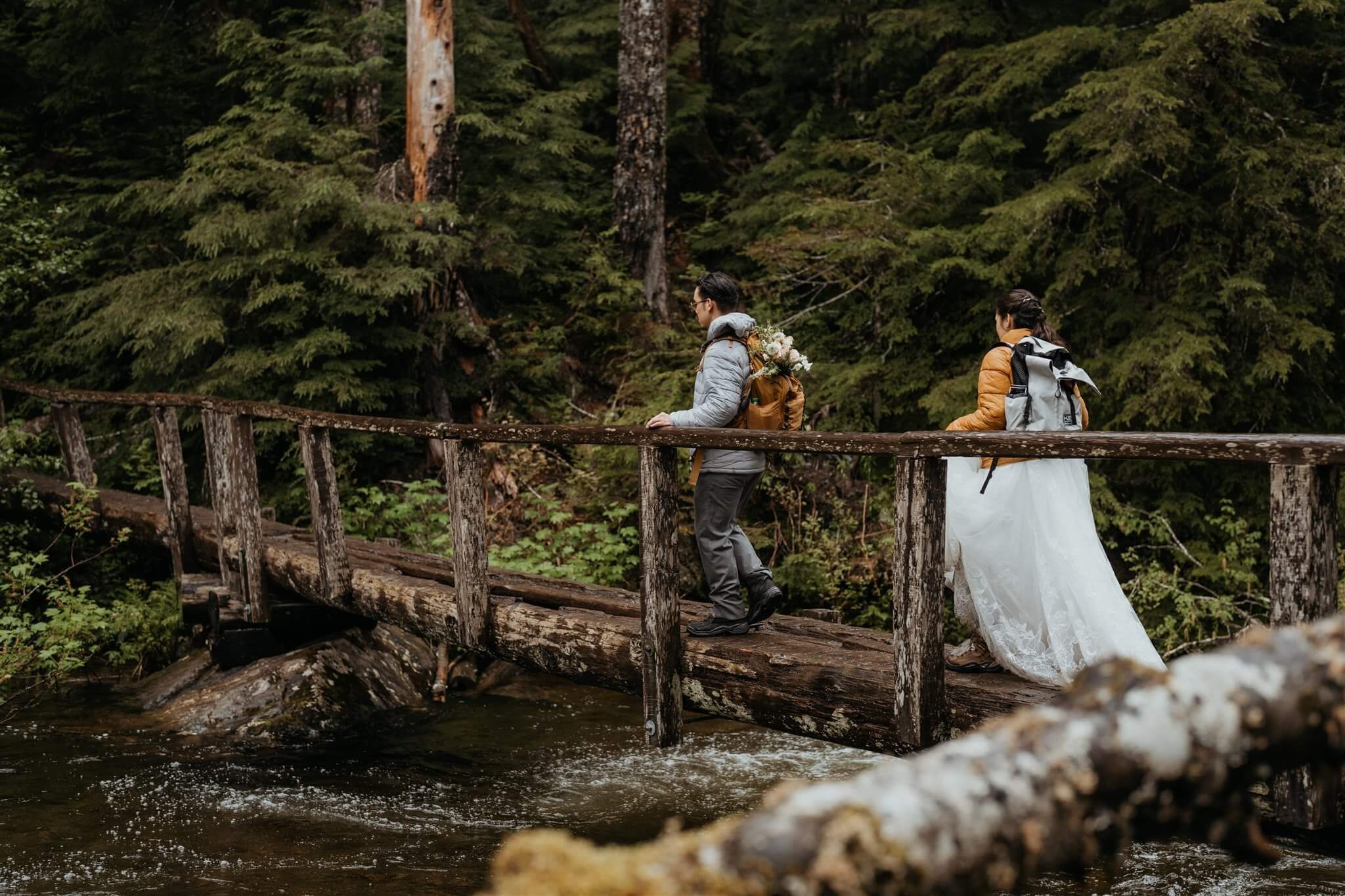 Bride and groom walk along a wood bridge over the river