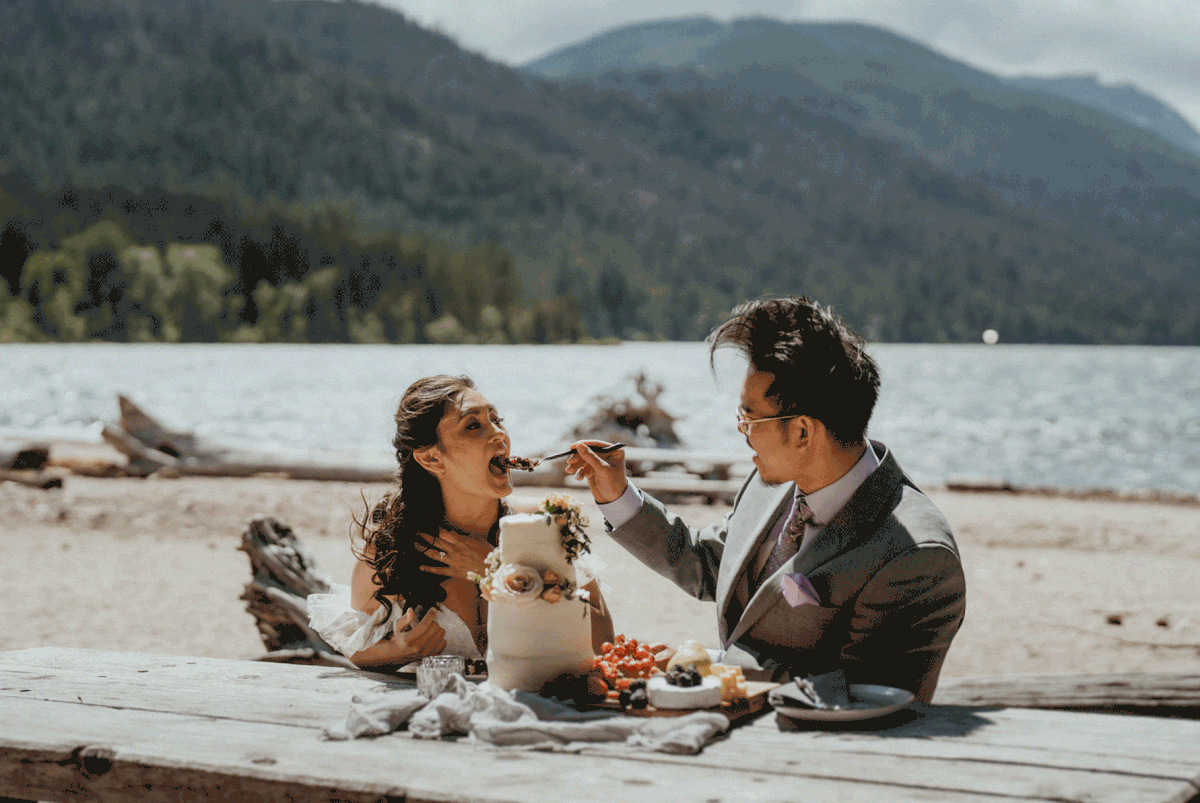 Groom feeds bride wedding cake by the lake
