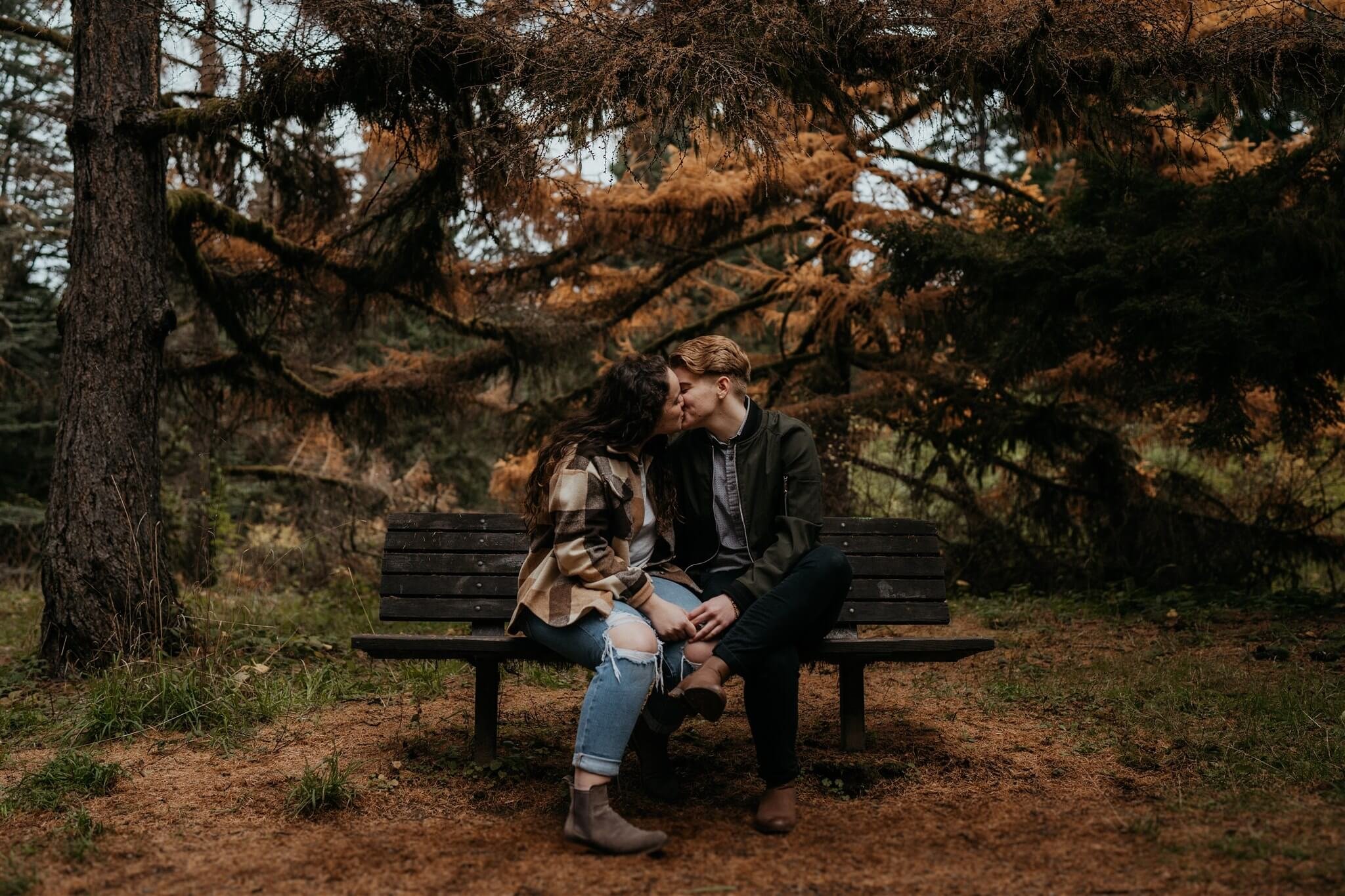 Two women kissing on a bench during Oregon engagement photos