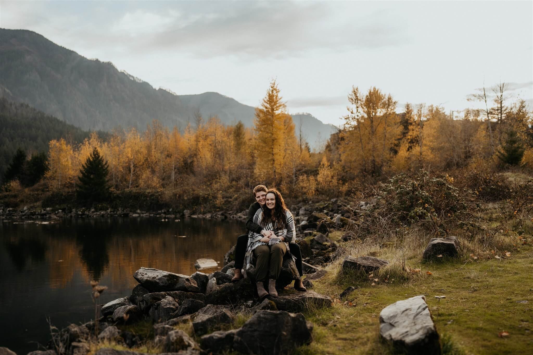 Two women sitting by a lake during Oregon engagement photos