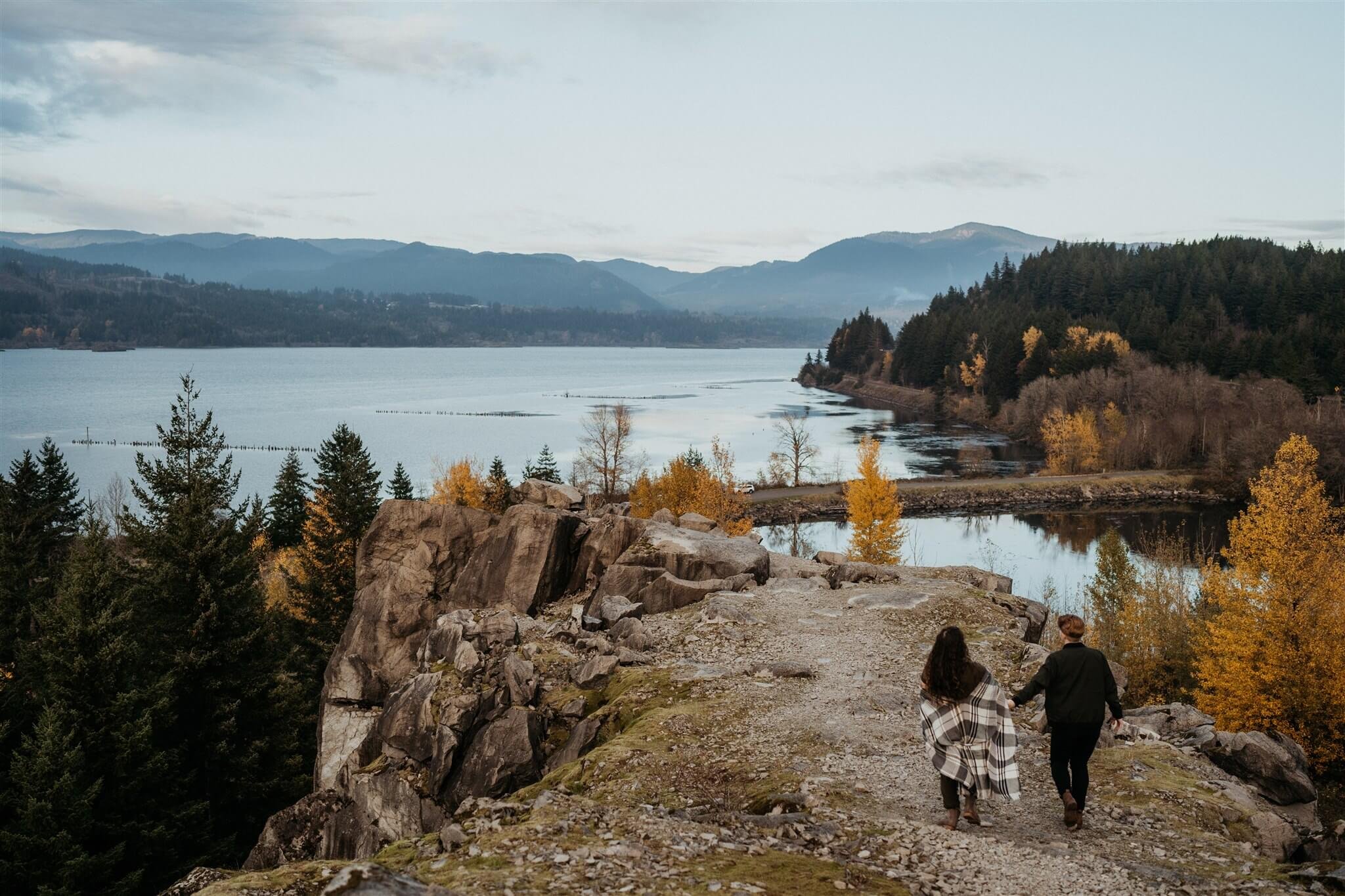 Couple holding hands, walking towards a lake during Oregon engagement