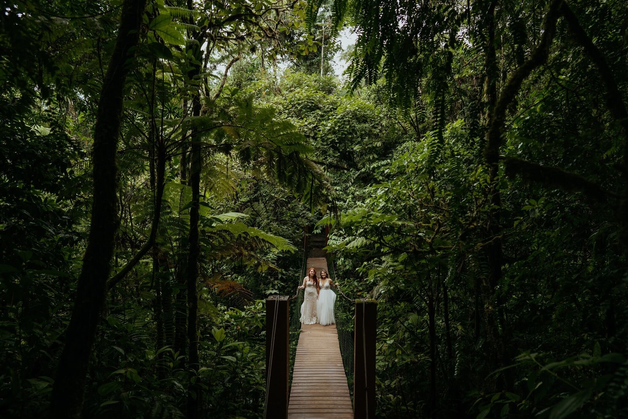 Two brides walk suspension bridge in the rainforest in Costa Rica