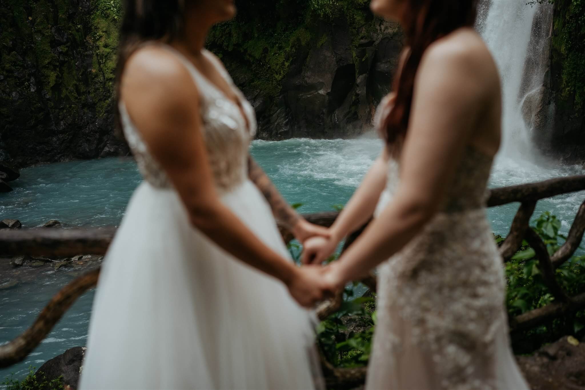 Two brides hold hands next to a waterfall during Costa Rica elopement