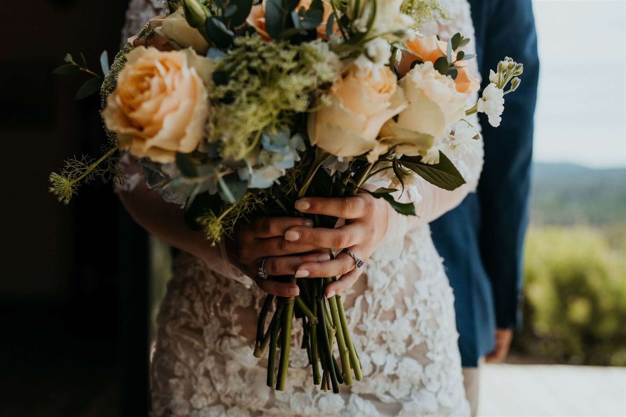 Bride holding peach, green, white, and blue floral arrangement
