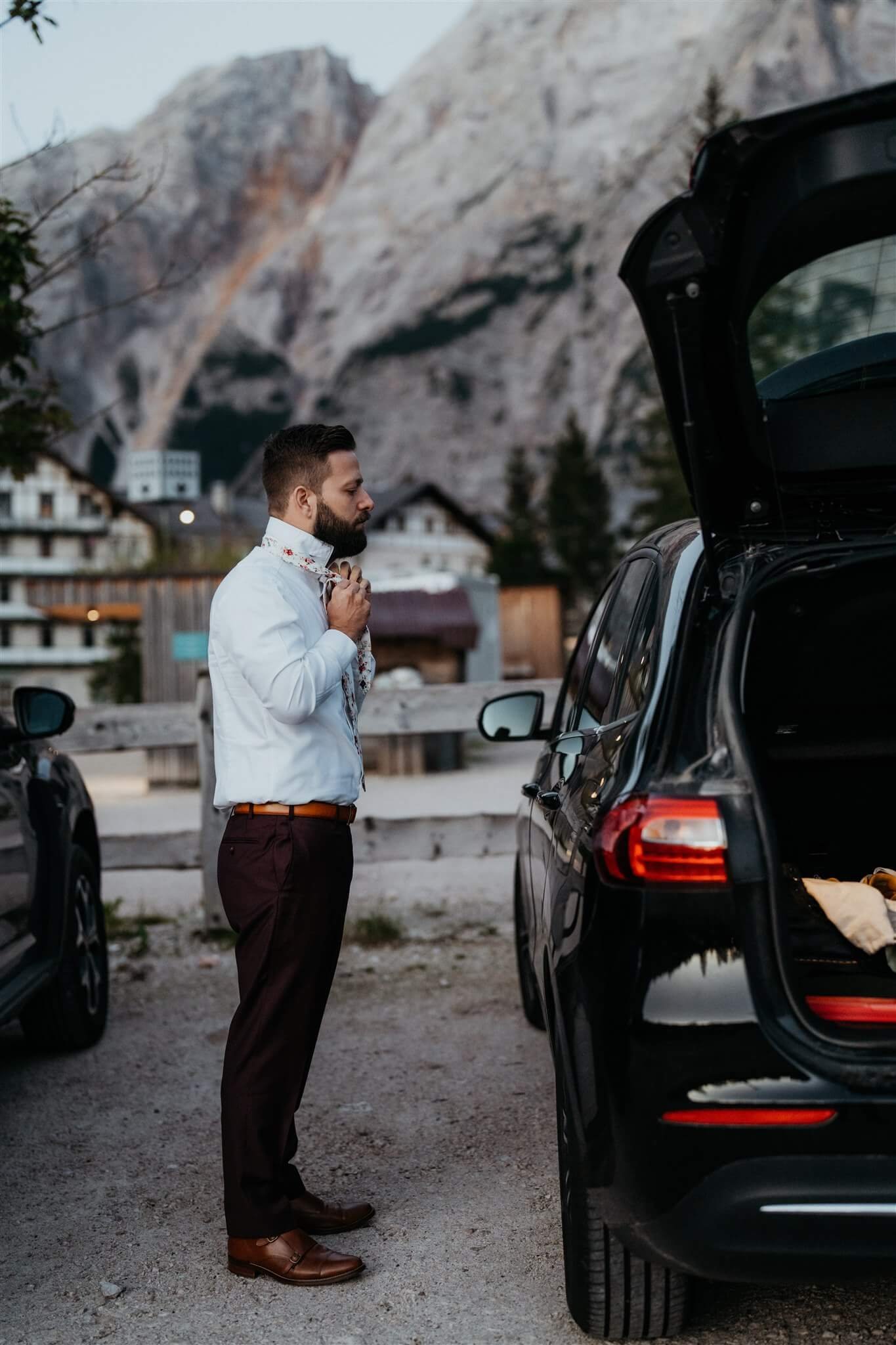 Groom adjusting tie next to car for sunrise vow renewal elopement in Italy