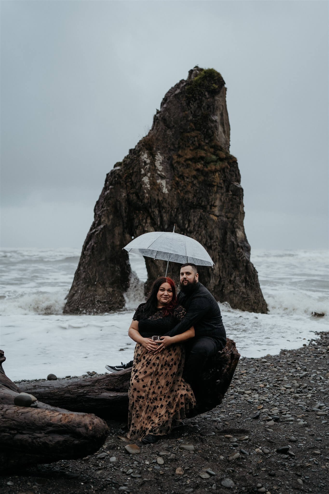Couple holding clear umbrellas during rainy engagement photos at Ruby Beach