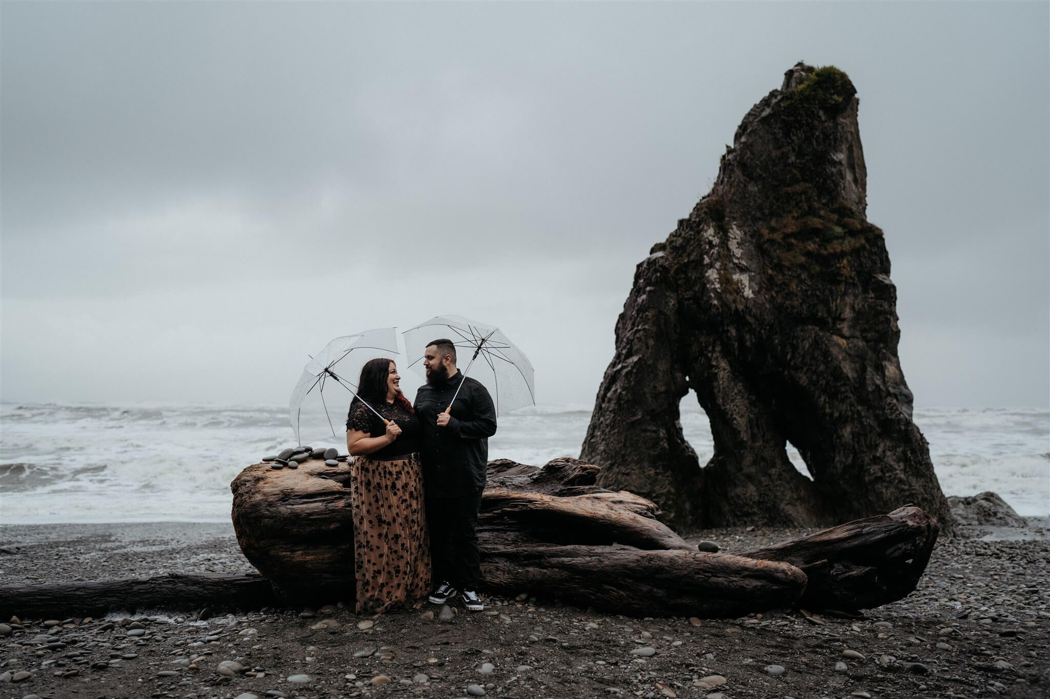 Couple holding clear umbrellas at Ruby Beach for Halloween engagement photo session