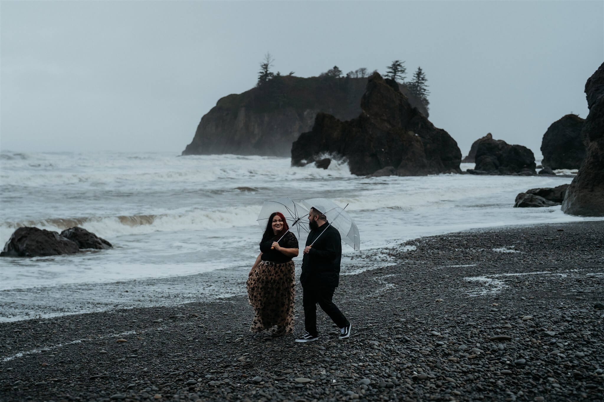 Couple holding clear umbrellas at Ruby Beach for Halloween engagement photo session