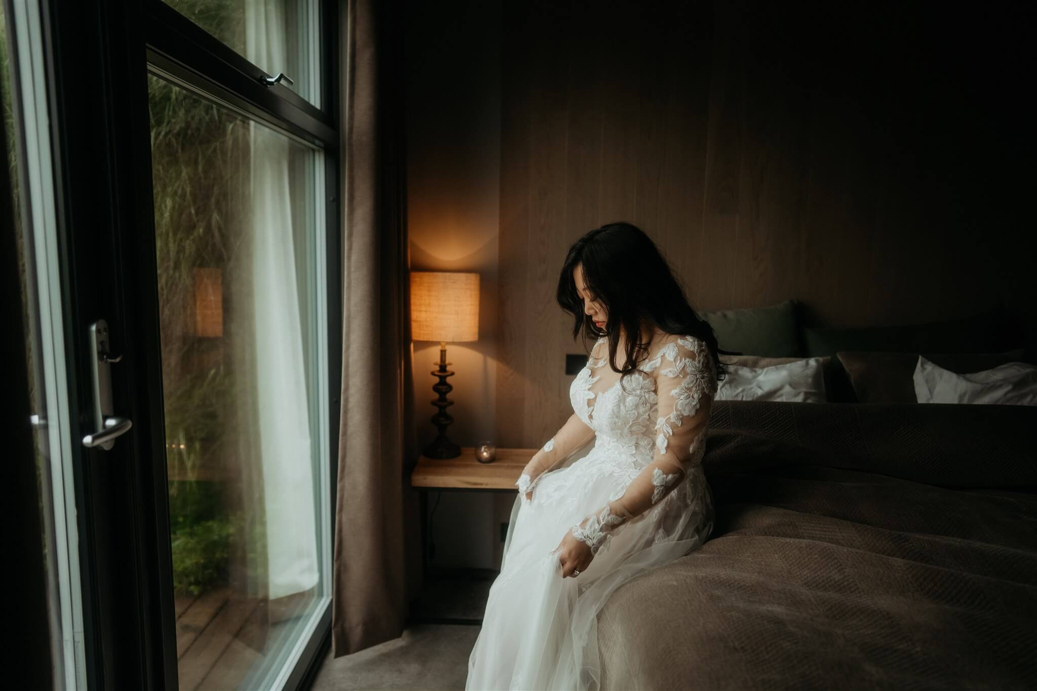 Bride sitting on the bed smoothing white wedding dress before eloping in Iceland