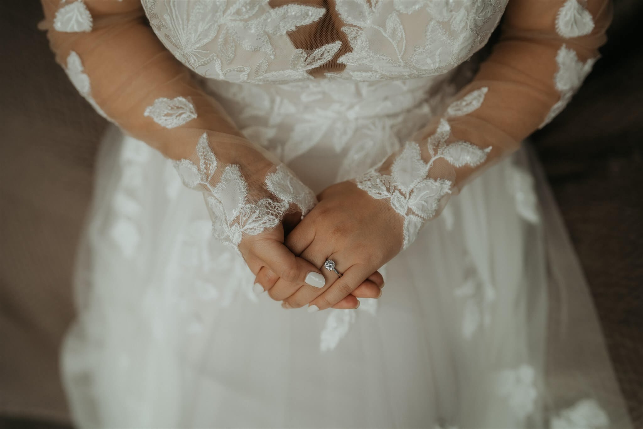 Bride folding hands on top of white lace wedding dress