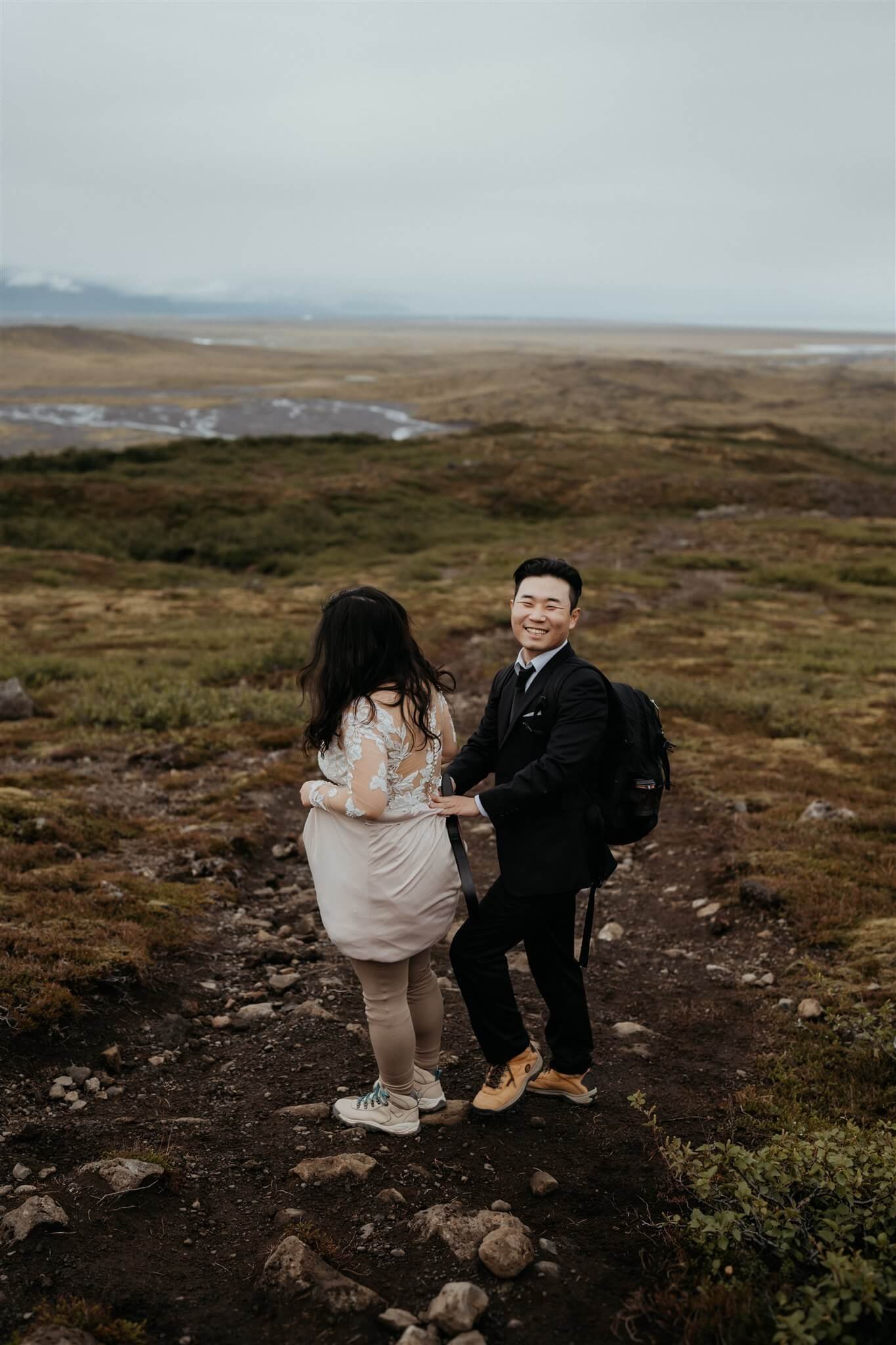 Groom helping bride with her wedding dress while they elope in Iceland