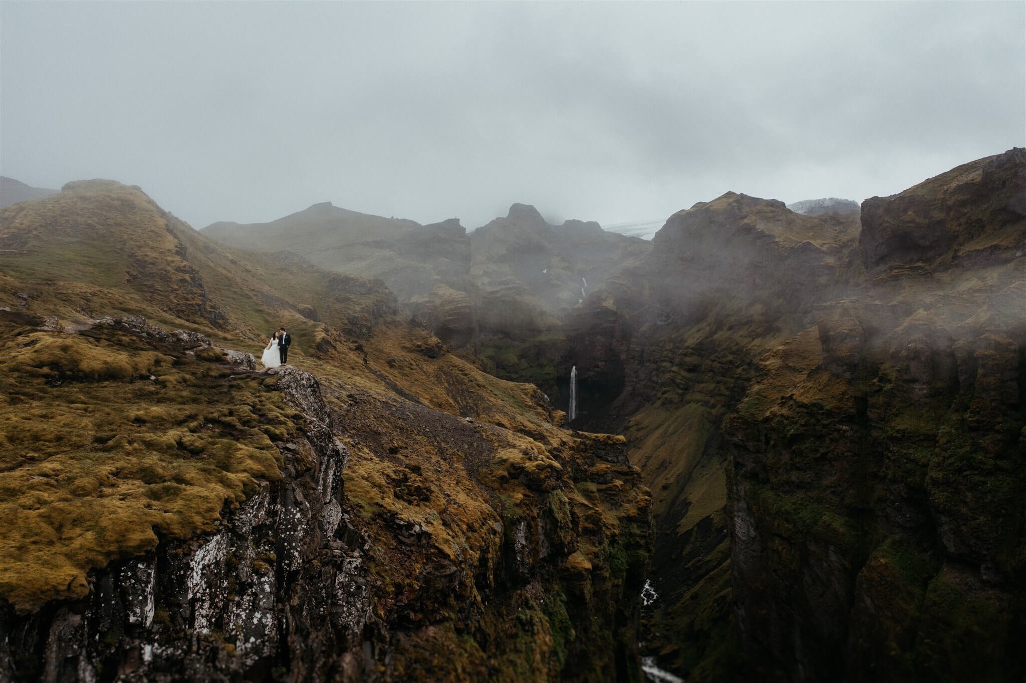 Bride and groom eloping on a cliff overlooking a canyon and waterfall in Iceland