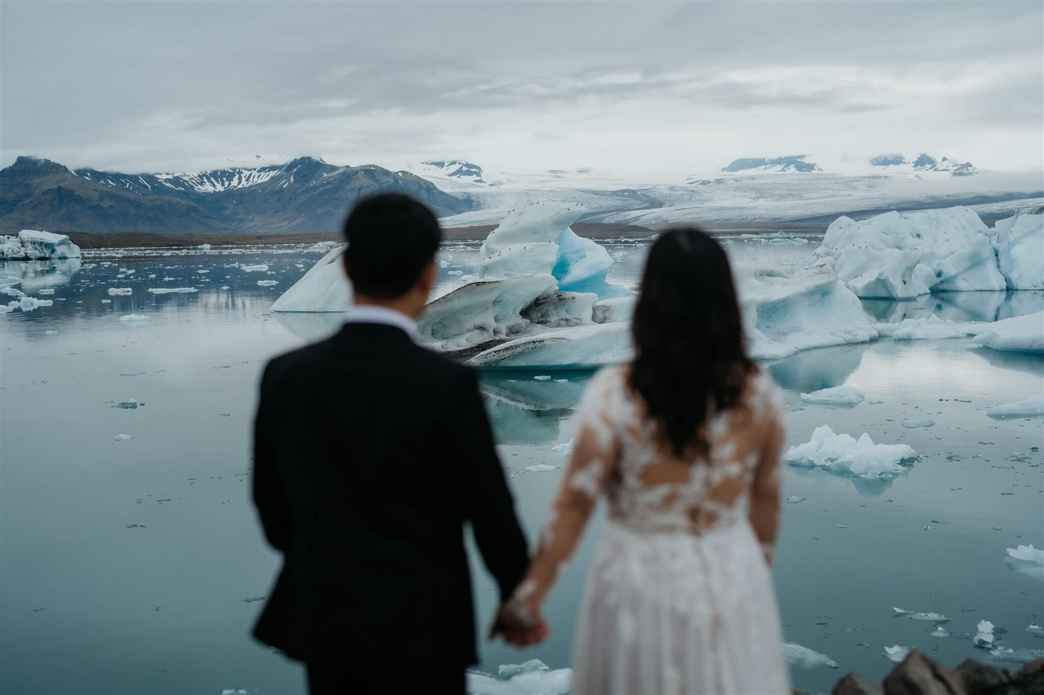 Bride and groom holding hands looking out into the icy water at their Iceland elopement