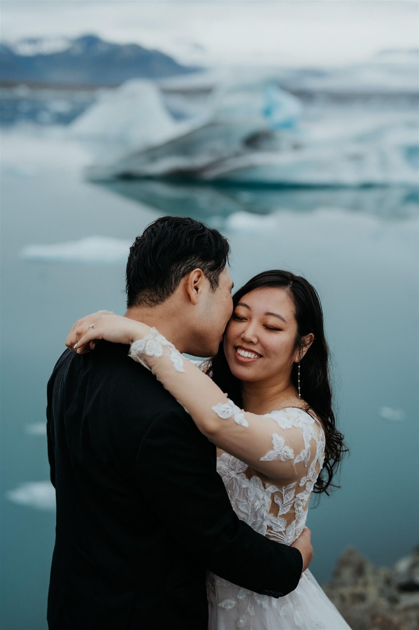 Bride and groom hug beside an icy lagoon during their elopement in Iceland